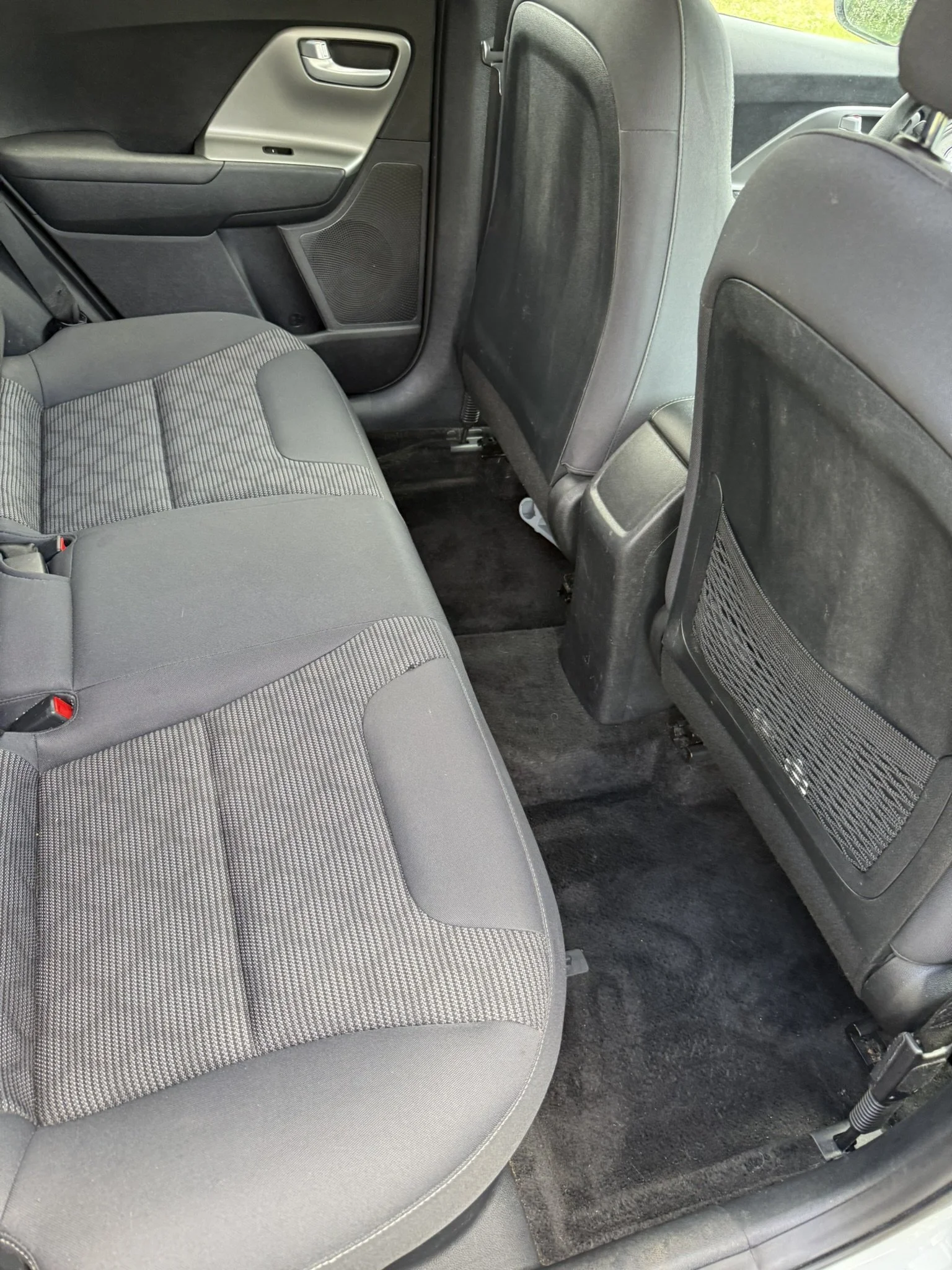 The backseat area of a vehicle showing a gray patterned cloth seat, black and gray interior door panel, and black floor carpet.
