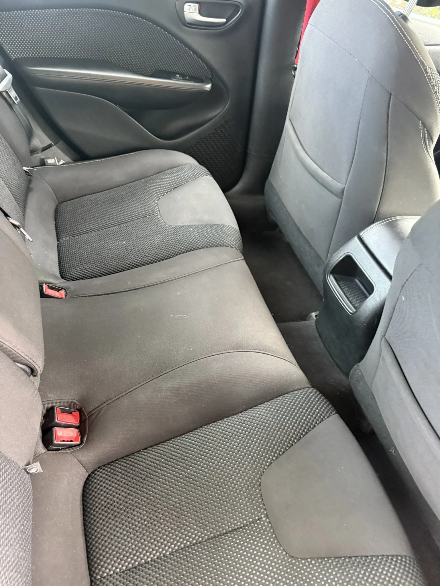 Backseat of a car showing fabric seats and seatbelt buckles.