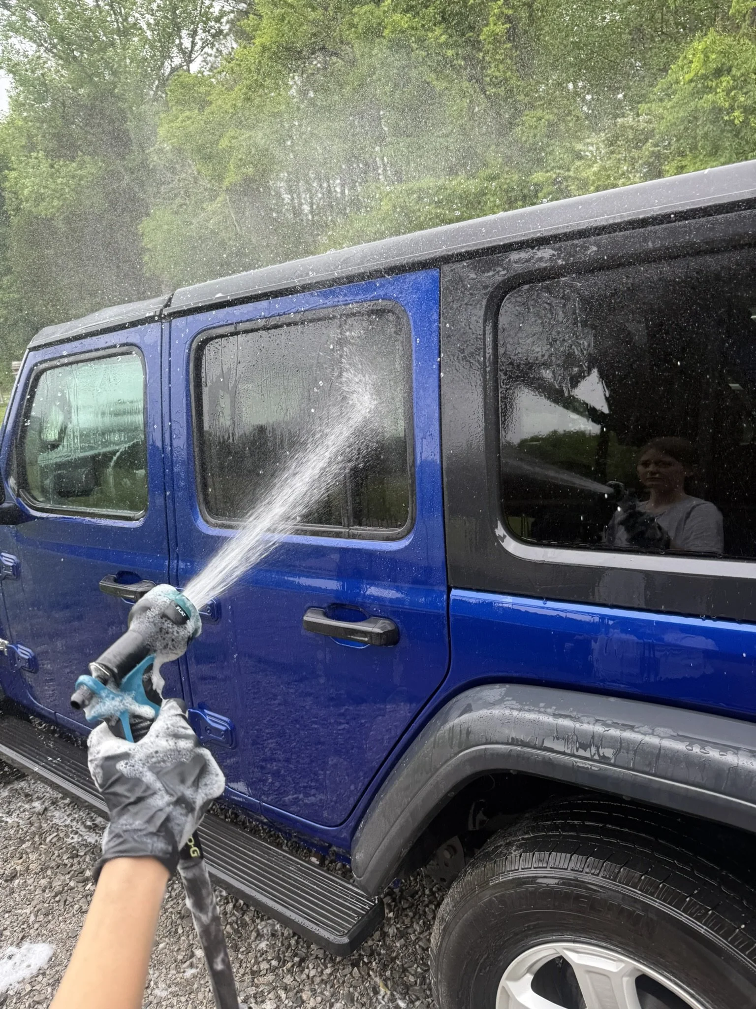 Person cleaning a blue pickup truck with a hose, soap, and water spray.