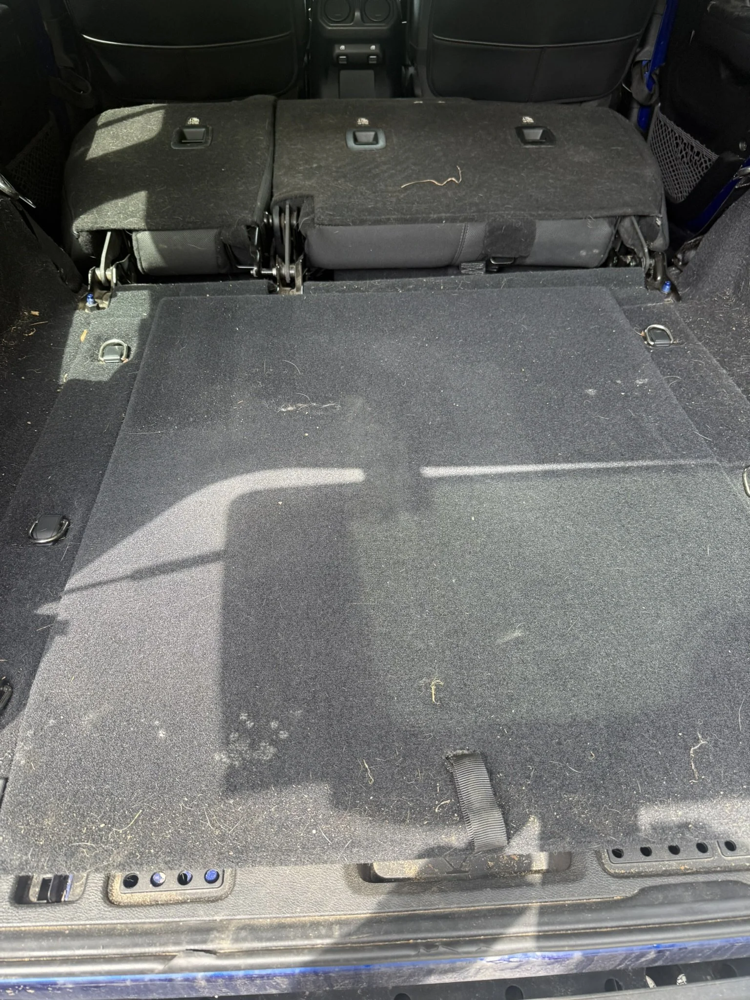 The back of a vehicle with the rear seats folded down, revealing an empty cargo space with some small debris and a strap at the bottom.