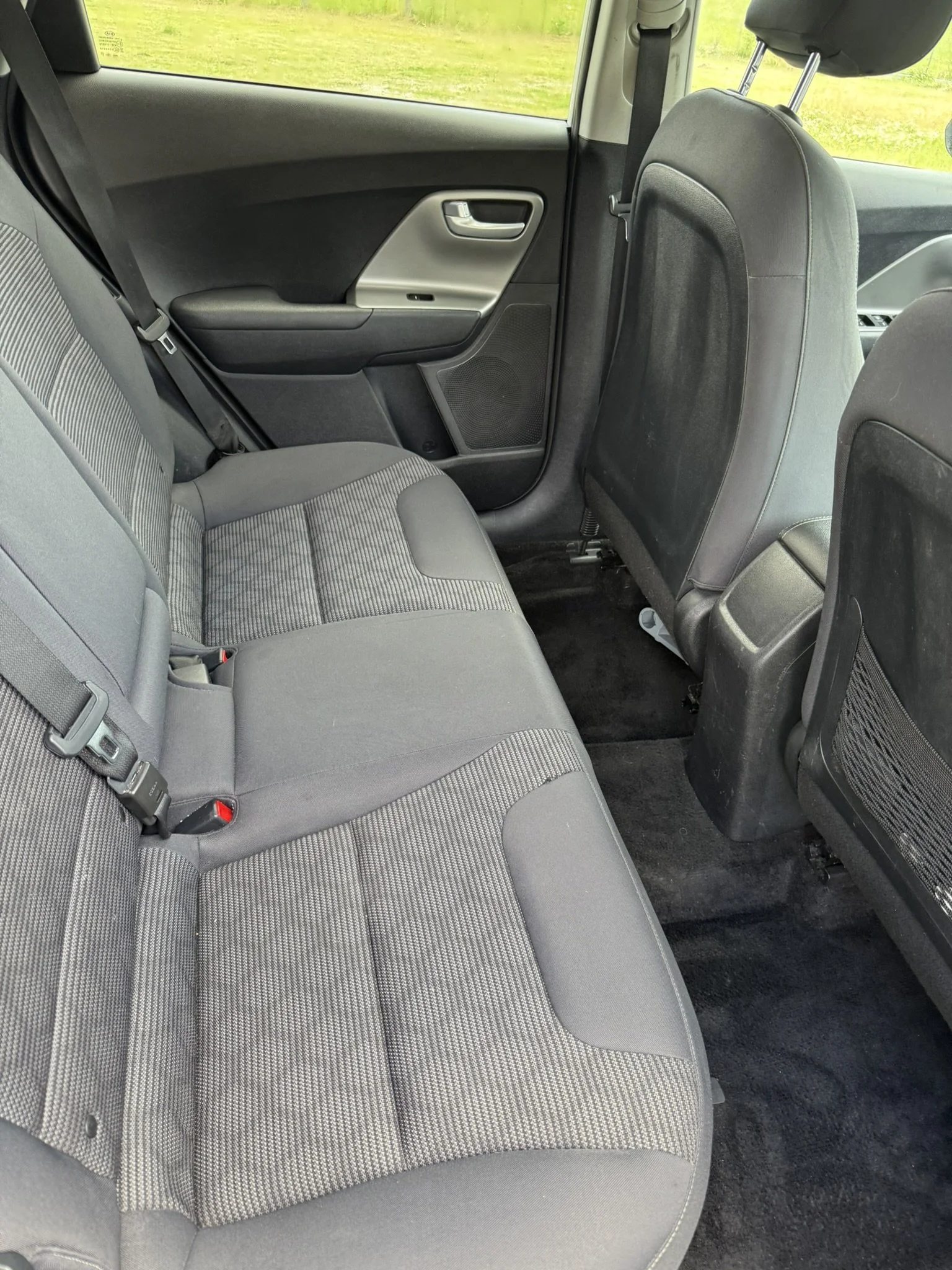 The backseat area of a car with fabric seats and a view of the exterior green landscape through the window.