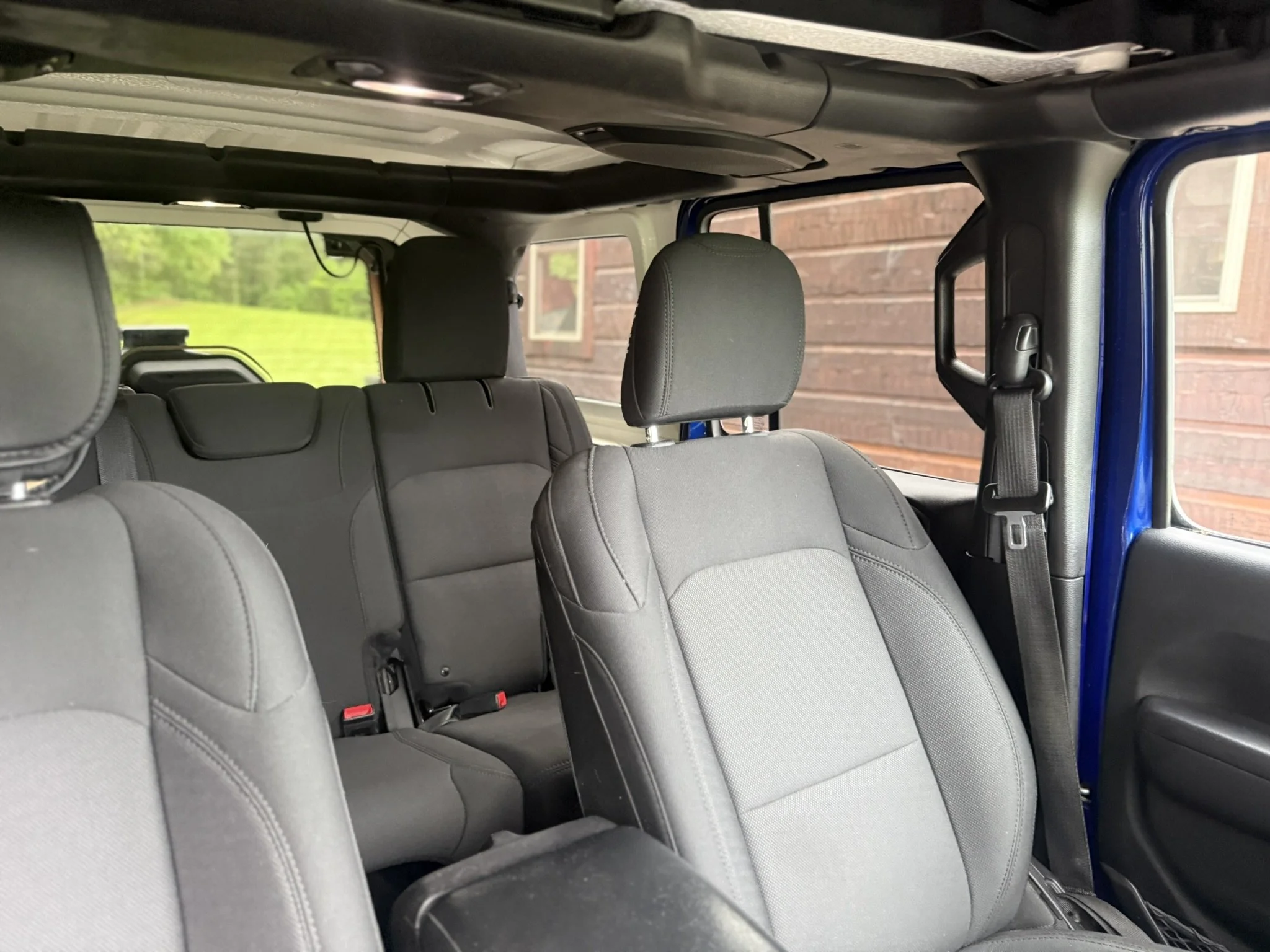 The interior of a blue vehicle showing gray fabric seats, headrests, seat belts, and a window with a brick building outside.