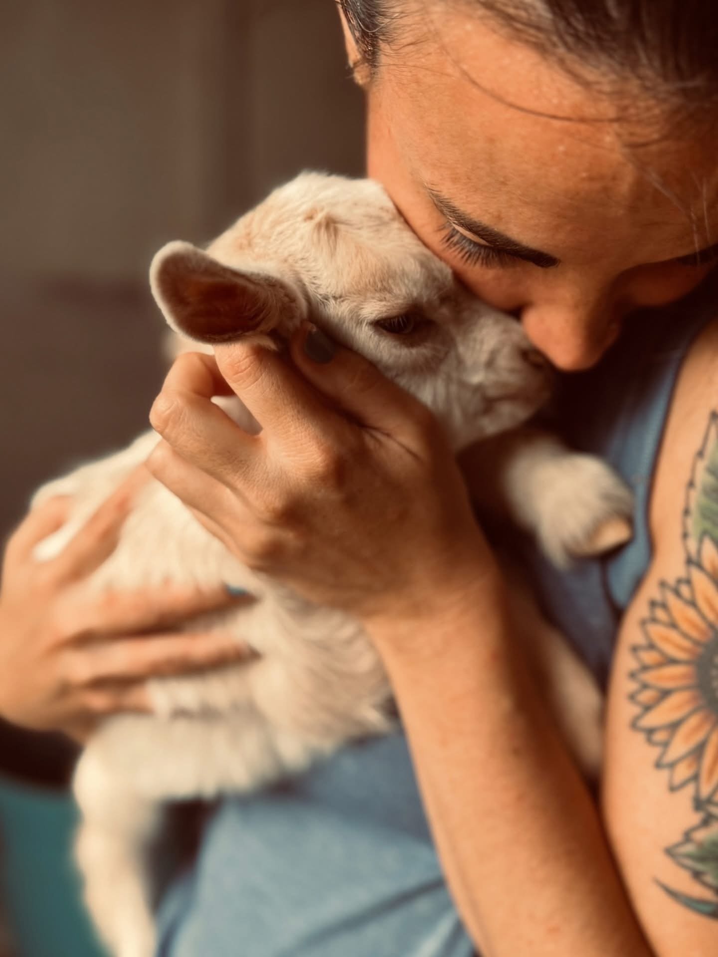 A person with tattoos holding and cuddling a small, light-colored puppy close to their face, showing affection.