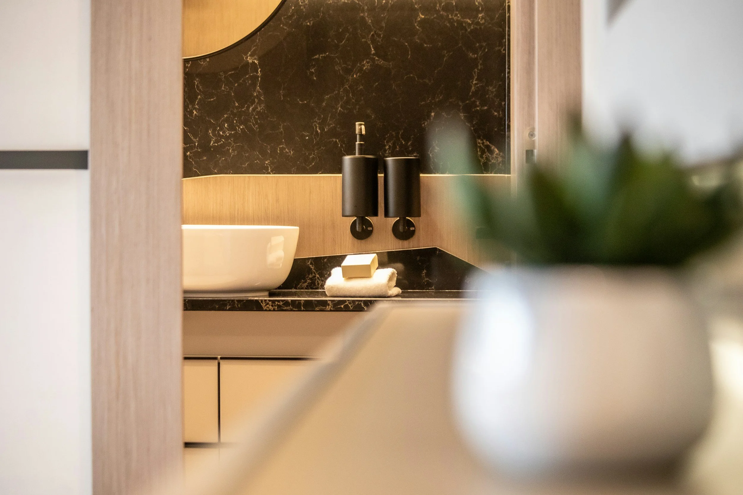 A bathroom sink with a bar of soap and a towel, reflected in a mirror with a dark marble wall background.