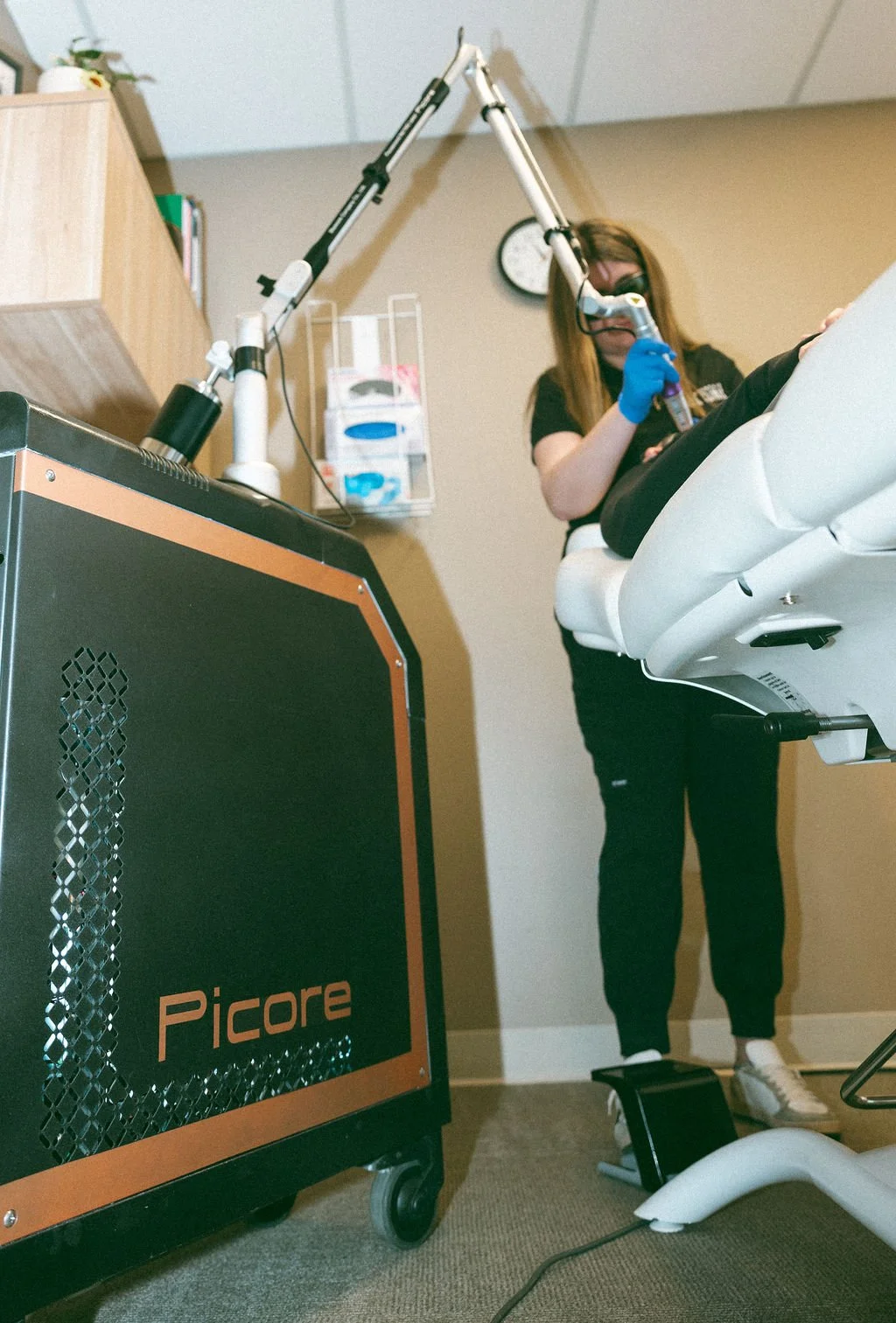 A dental professional using a laser device during a dental procedure on a patient lying in a dental chair, with dental equipment nearby.