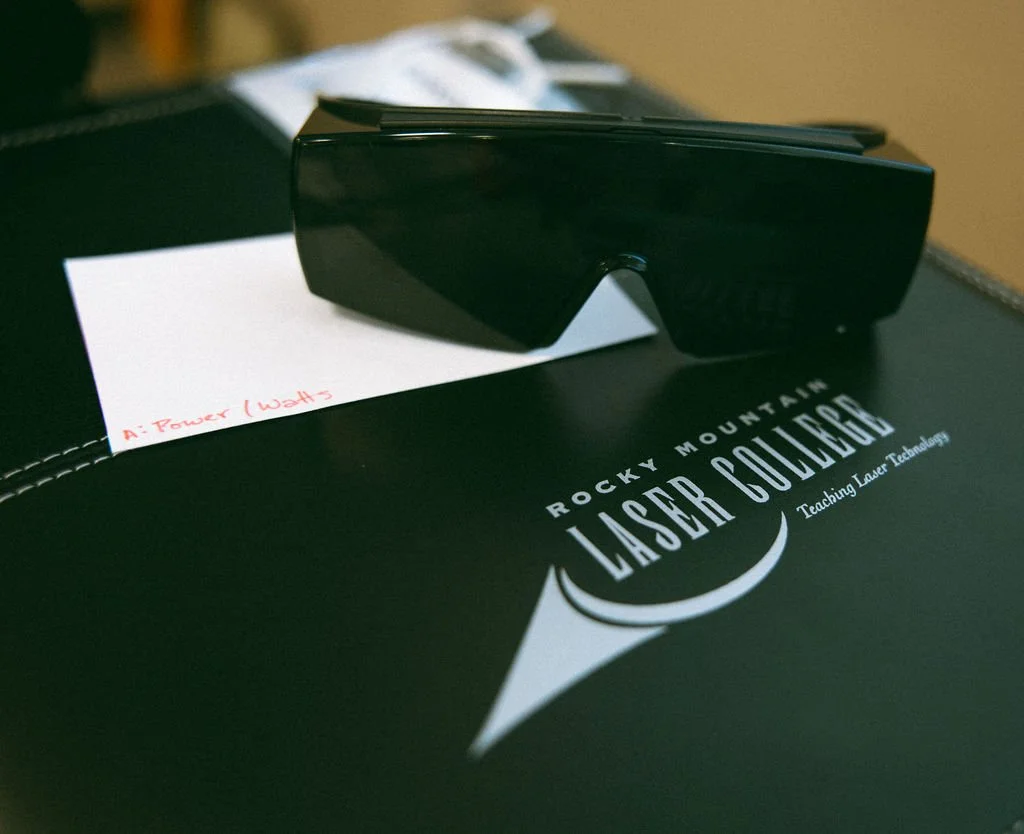 A pair of black laser safety glasses resting on a black Rocky Mountain Laser Combobration box with the logo and the slogan 'Teaching Laser Technology'.