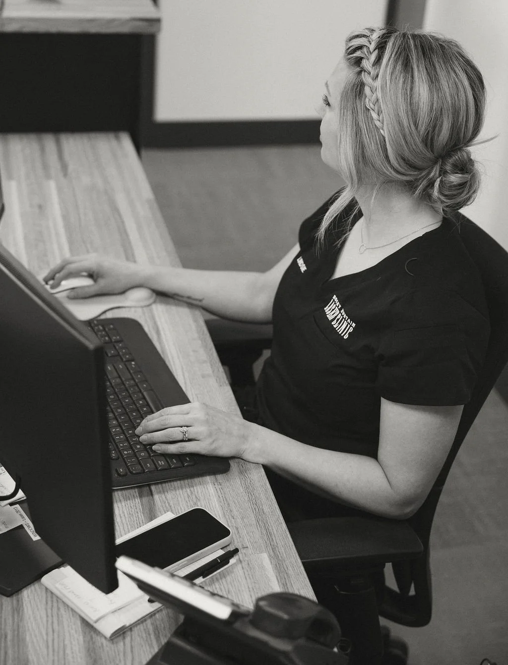 A woman with blonde hair styled in a braid and bun, sitting at a desk, working on a computer.