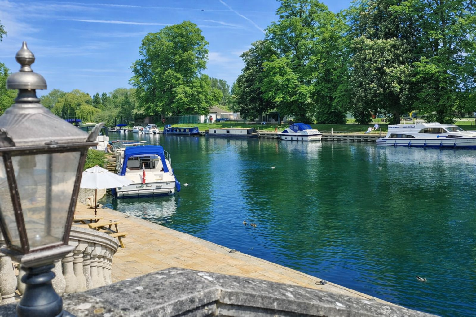 Calm waterway with docked boats, lush green trees, and a partly cloudy sky.