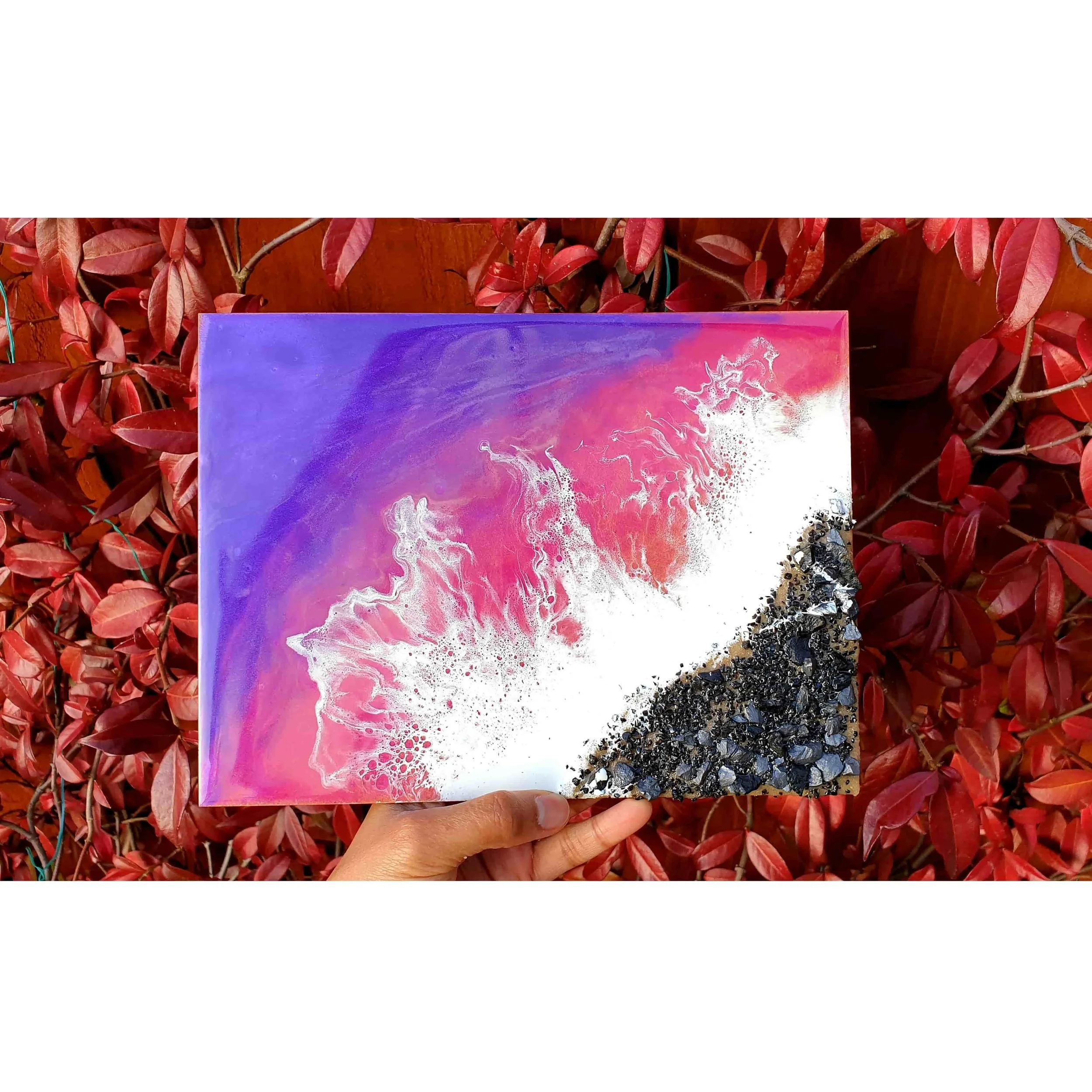 A person holding a colorful abstract painting with swirls of purple, pink, and white, in front of a background of red leaves.