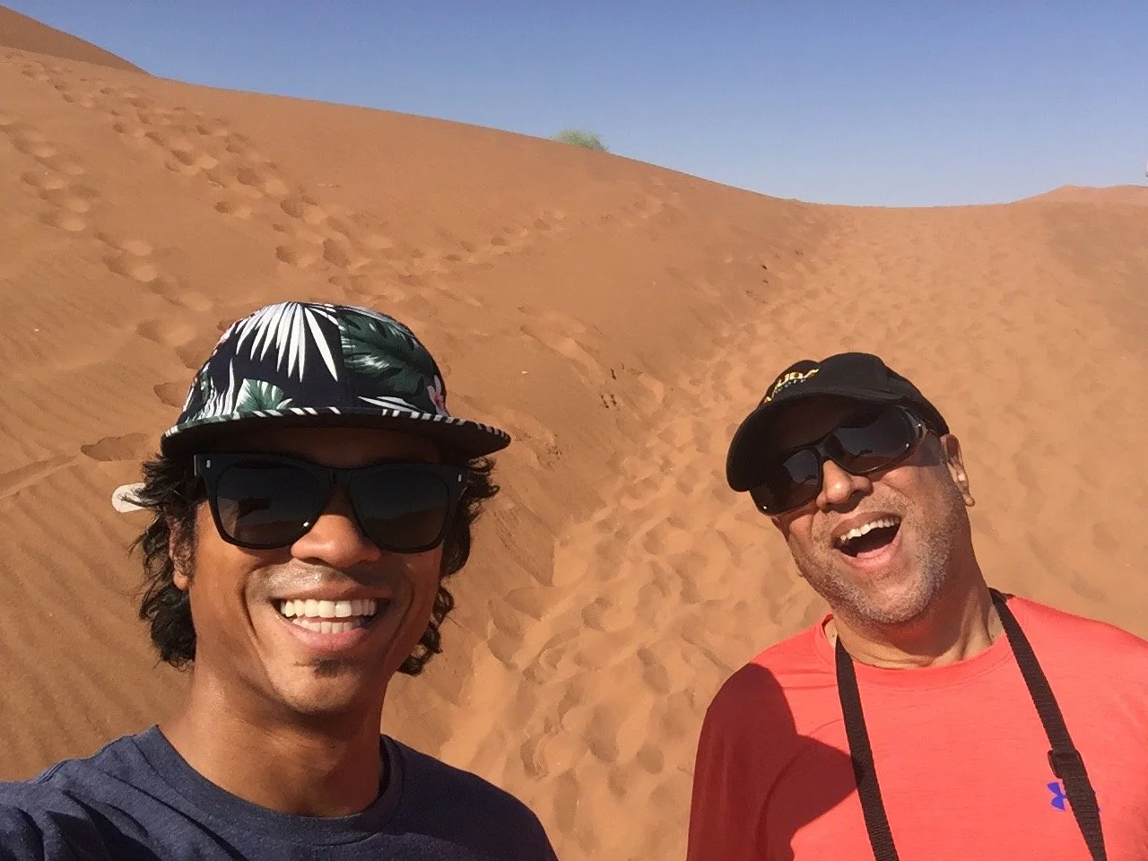 Neil and his father laughing together in a selfie in front of red sand dunes in Namibia.