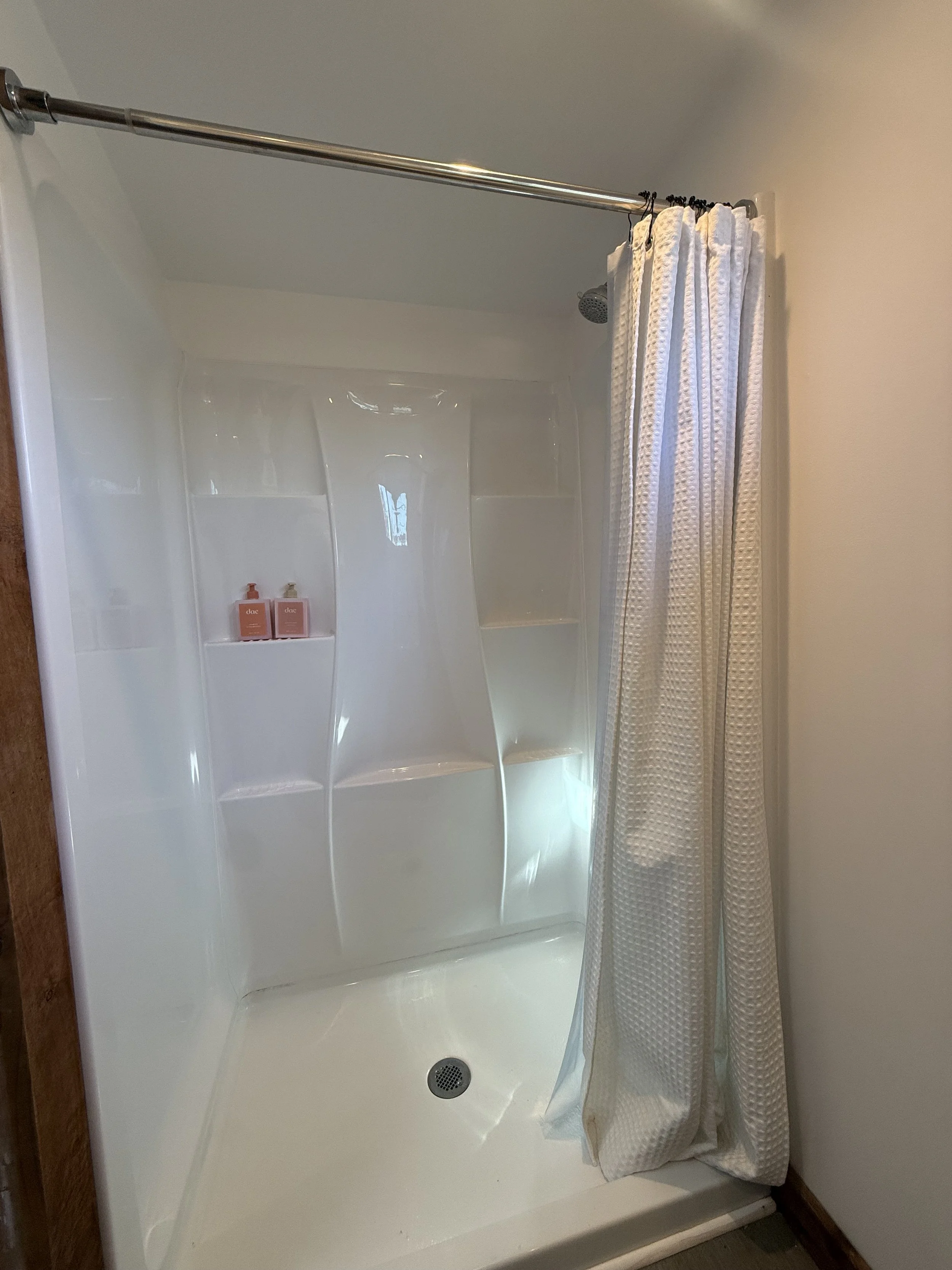 Clean shower with white walls, a showerhead, shampoo bottles, and a fabric curtain.