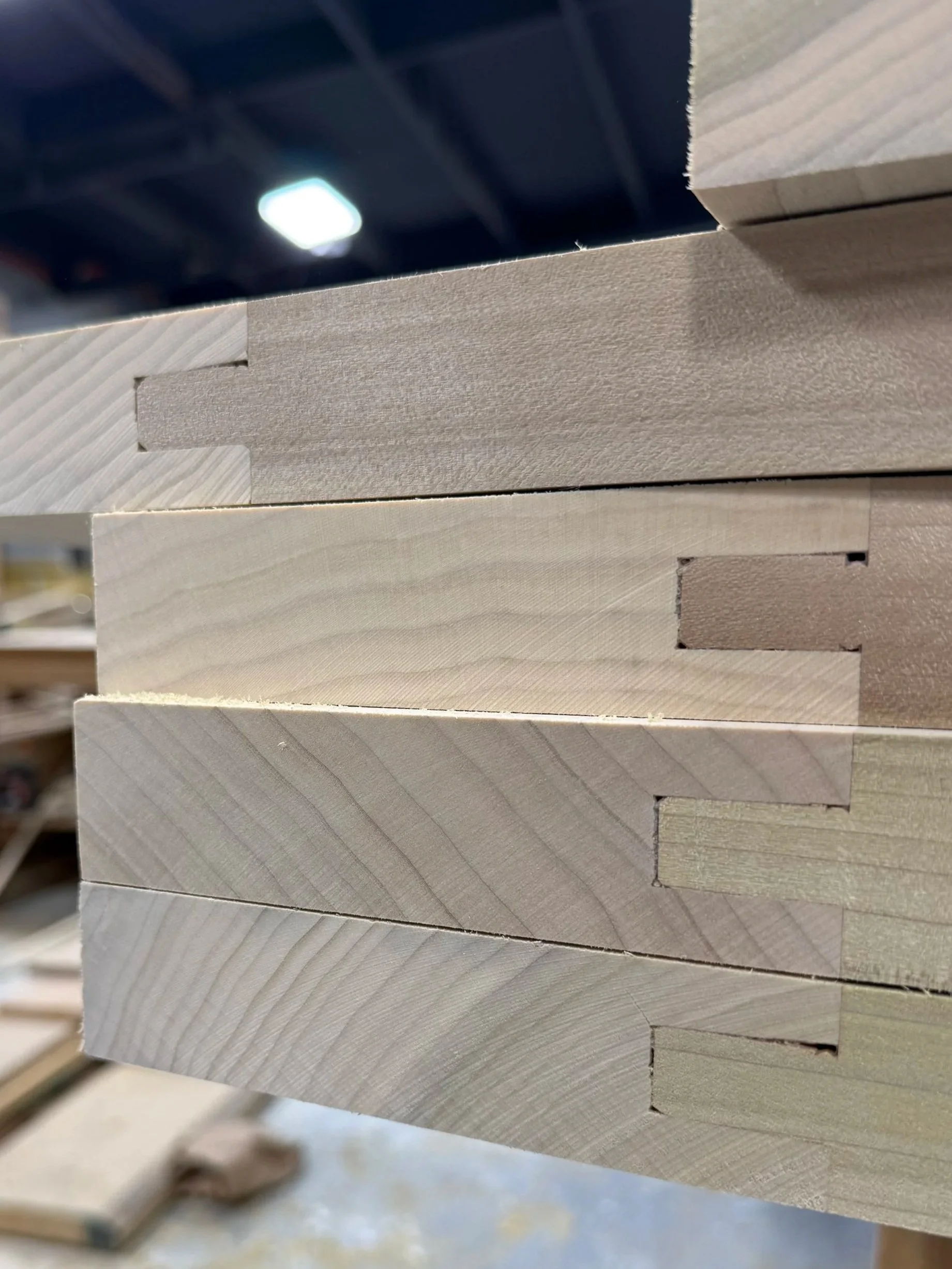 Stacked cut wooden planks with visible grain patterns in a woodworking or construction setting.