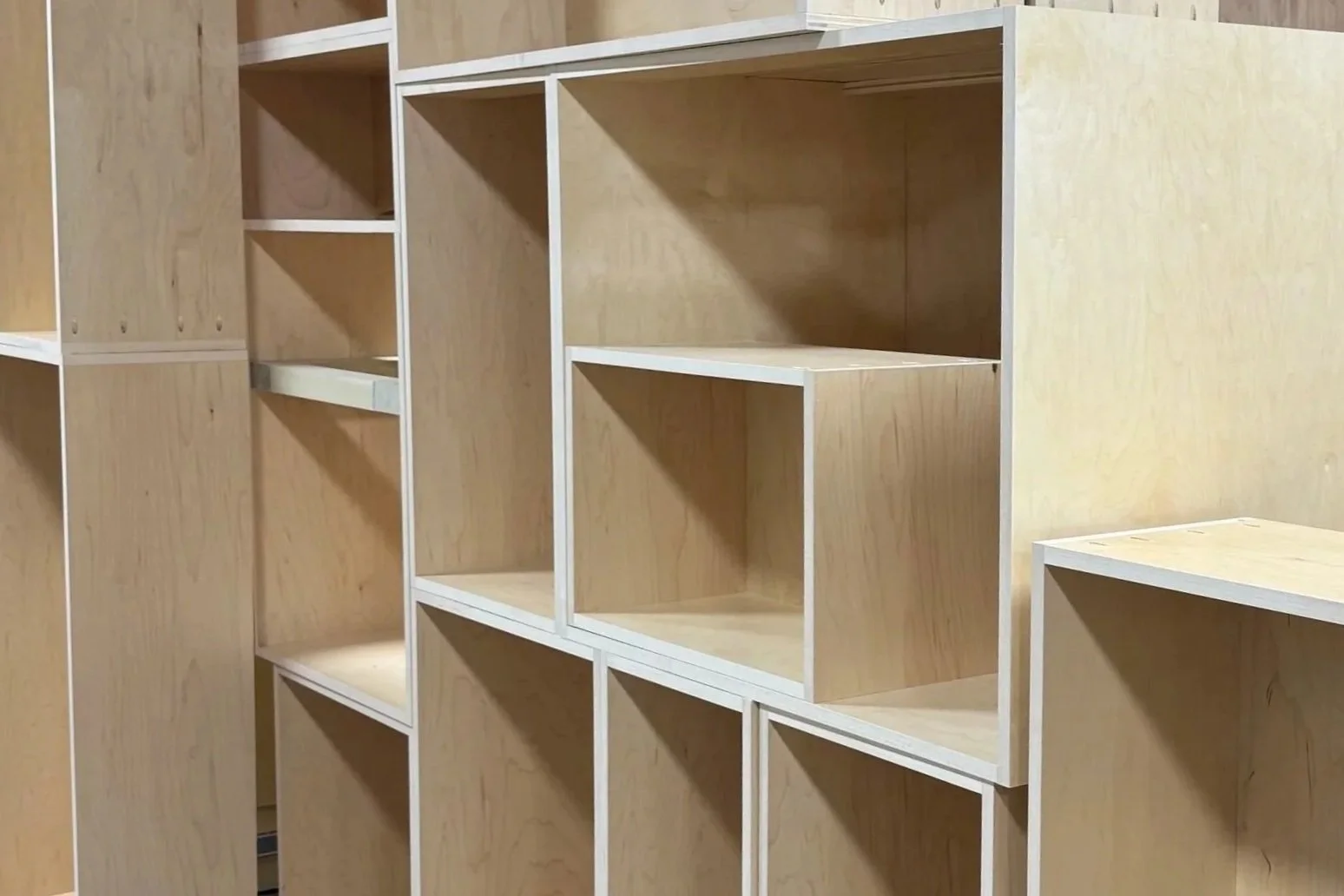 Empty wooden shelves with white framing, part of a modular storage unit against a wooden wall.