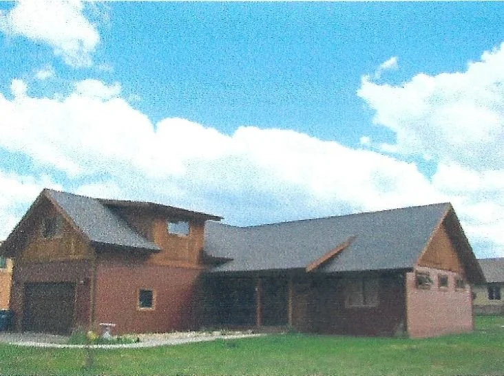 A wooden house with a multiple rooflines against a partly cloudy blue sky.