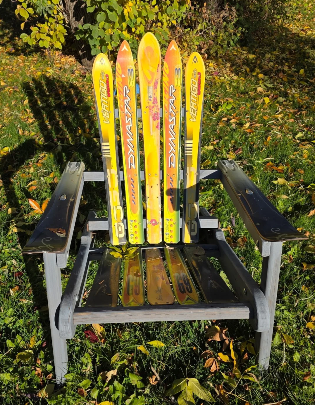 A custom folding wooden adirondack chair made of orange and yellow skis outside