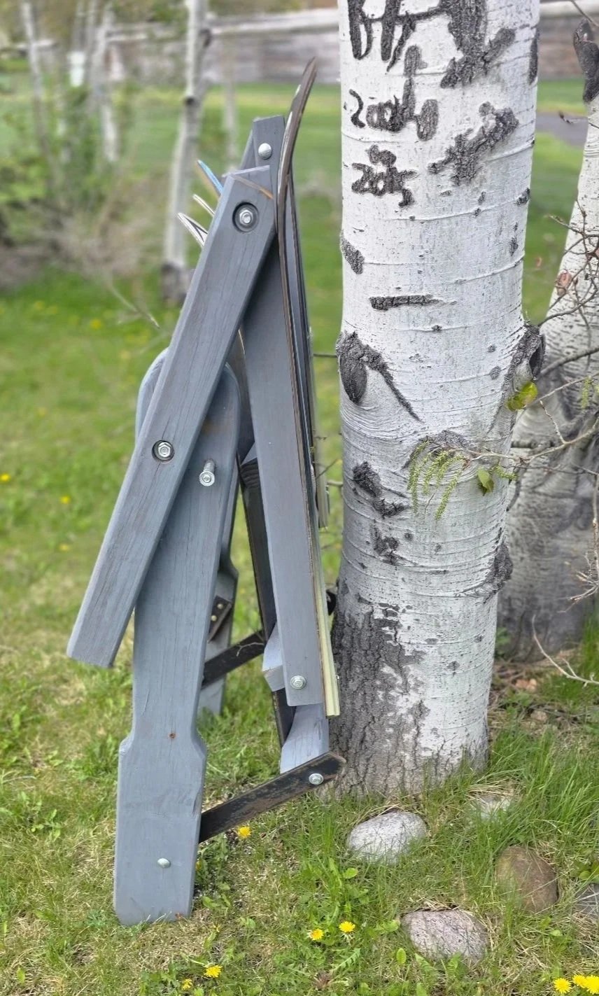 A folding wooden adirondack chair made of old skis leaning against an aspen tree.