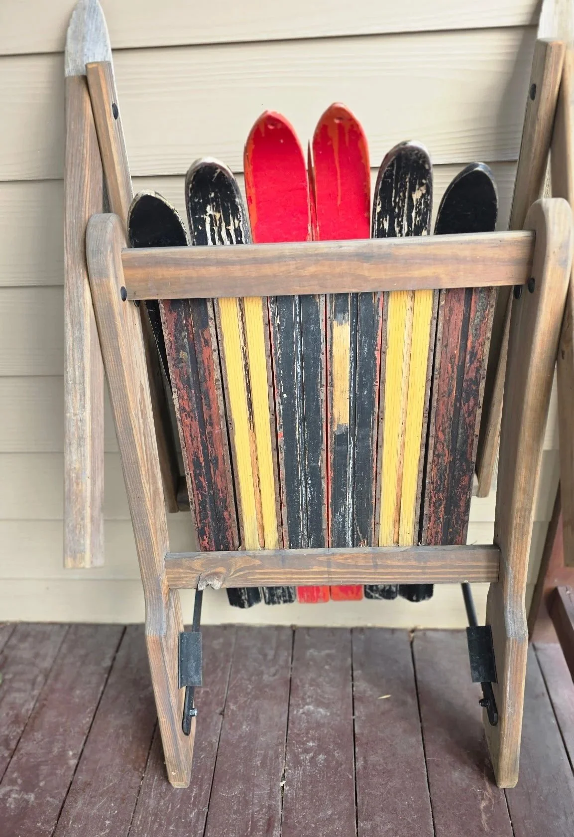 A vintage adirondack folding chair using antique skis, folded and leaning against a porch wall.