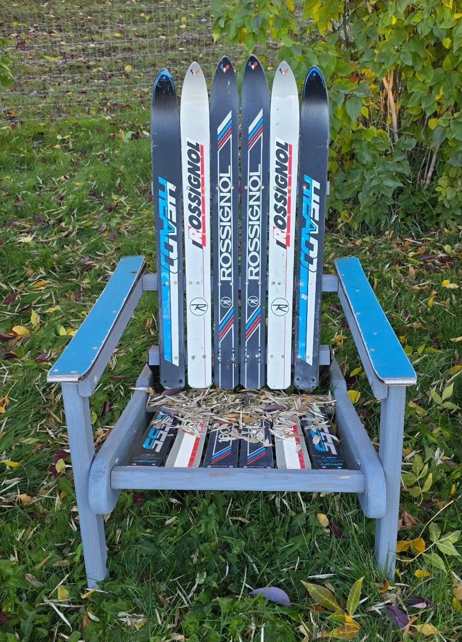 A folding wooden adirondack chair made of with five skis, a mix of black, white, blue retired skis, "Rossignol" visible on some of the skis.