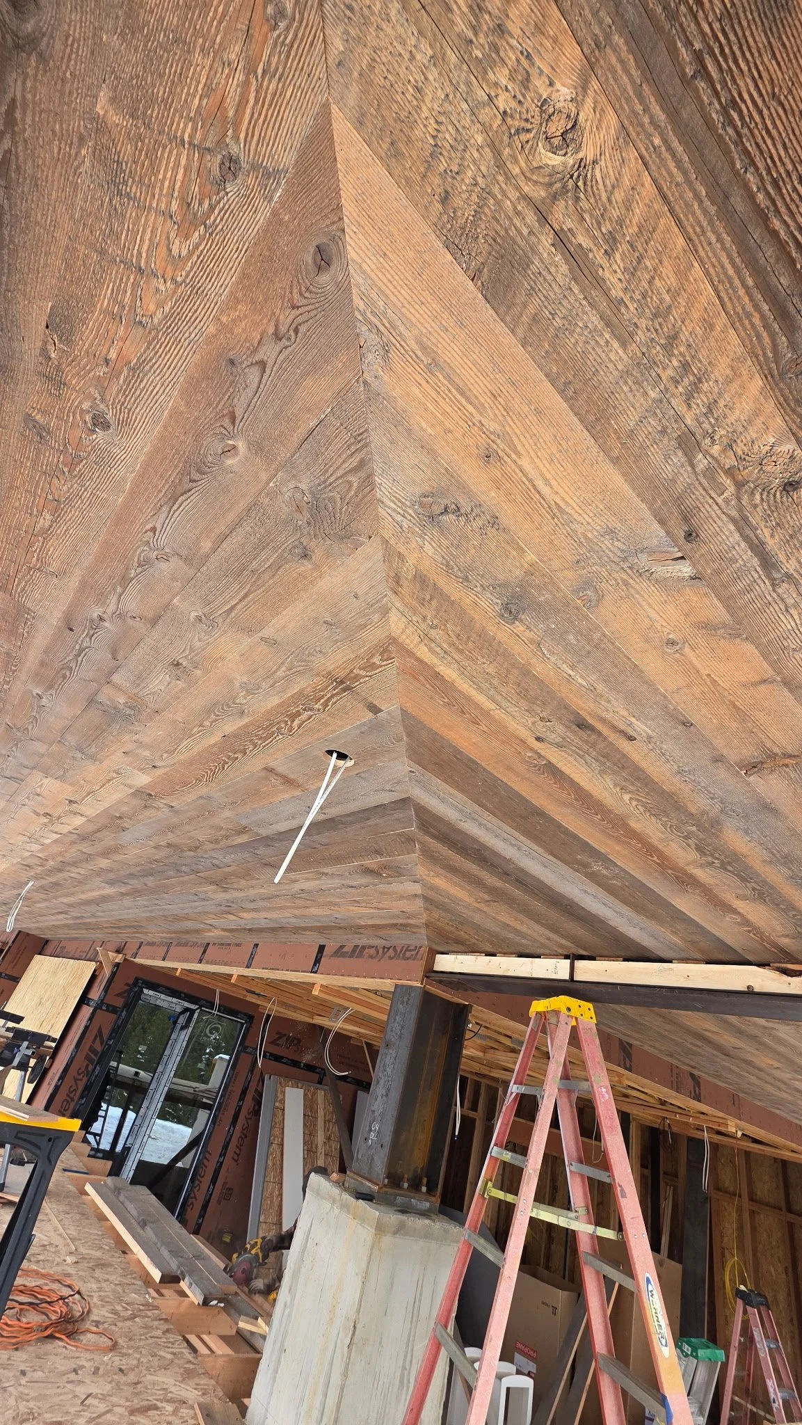Construction site with wooden ceiling, ladder, and construction materials inside a house under renovation.