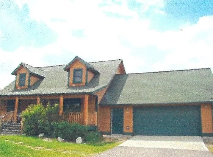 A two-story house with a wooden exterior, front porch, and a two-car garage under a cloudy sky.