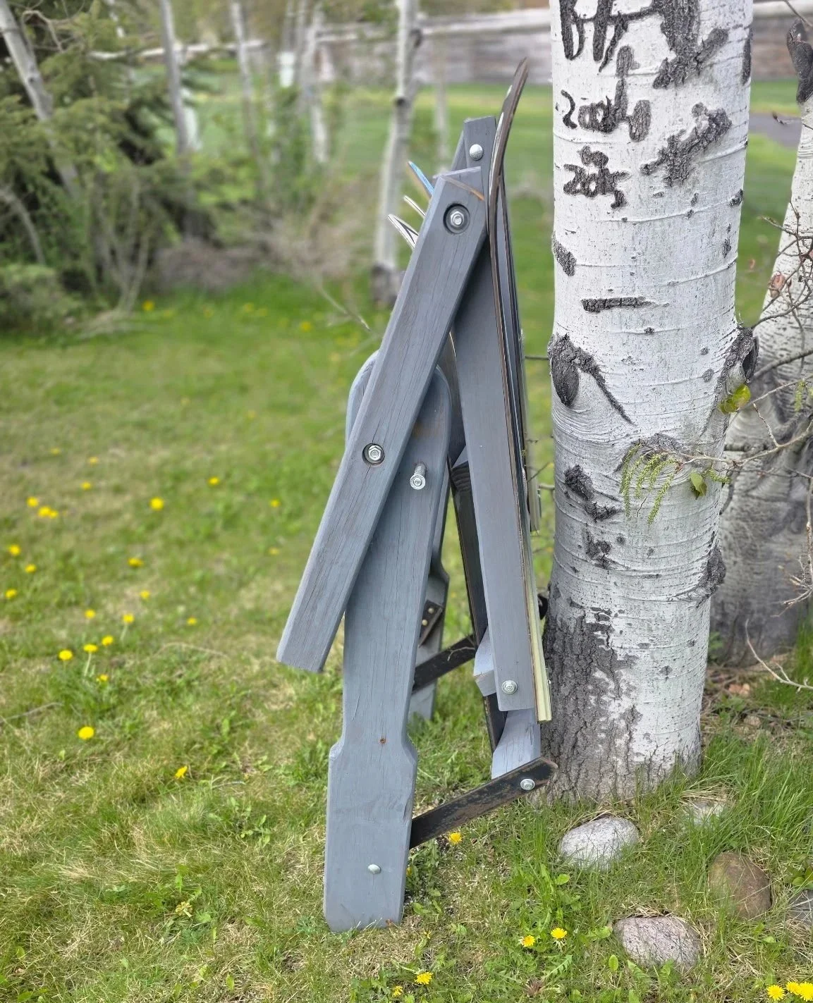 Folded custom adirondack wood chair made of skis leaning against an aspen tree.