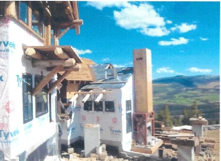 Construction site with buildings under construction, some wrapped in Tyvek house wrap, with mountains and blue sky in the background.