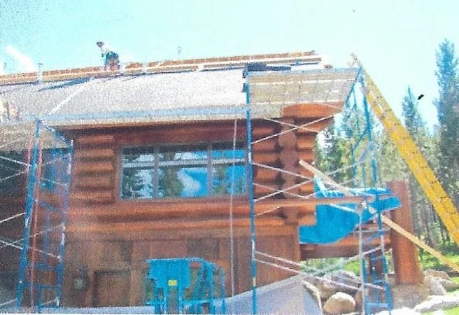 Log cabin under construction with scaffolding, a construction lift, and a partially completed roof.