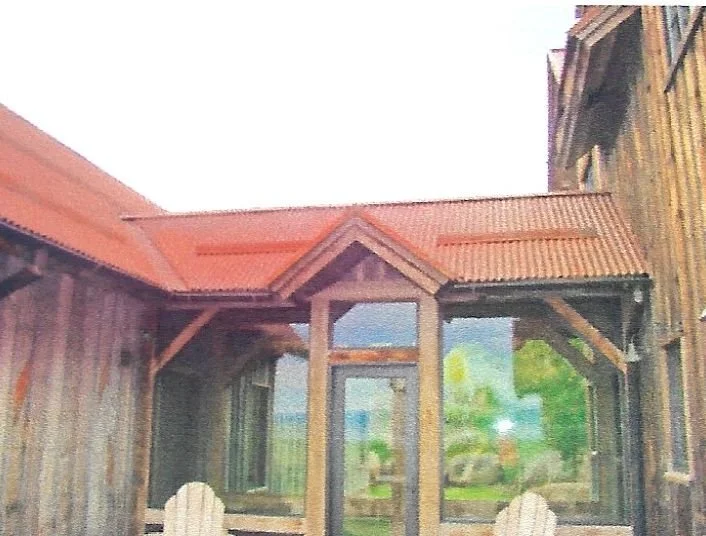 Exterior of a rustic wooden house with a small porch and glass windows, surrounded by trees.