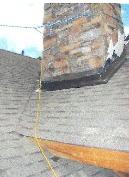 Close-up of a brick chimney on a roof with a black flashing and a yellow cord hanging from it.