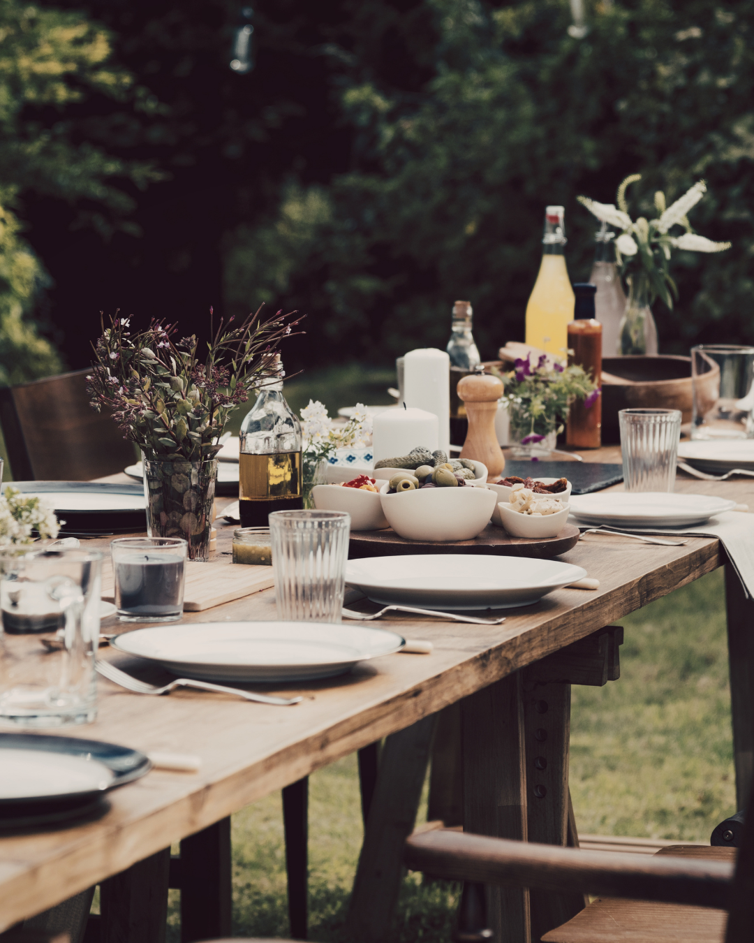 Elegantly set outdoor dining table with white plates, wildflowers, and small dishes ready for a celebration meal