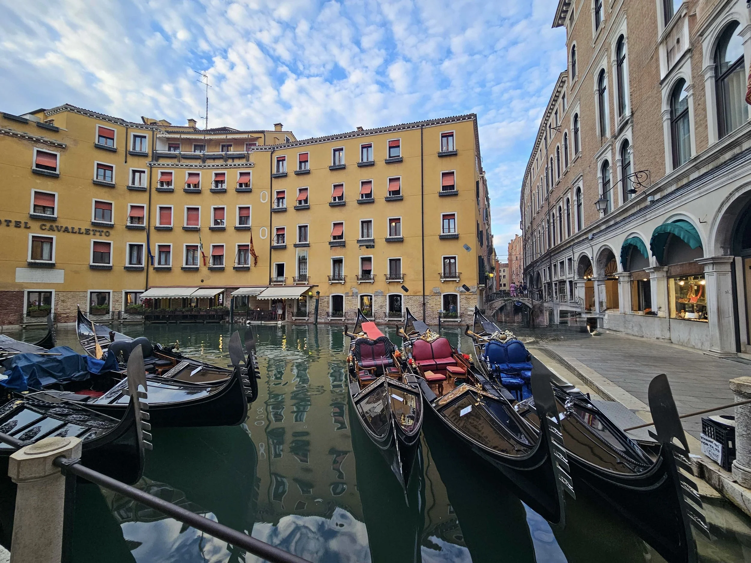 Black gondolas moored on a calm Venice canal lined with warm ochre buildings and arched walkways, Italy
