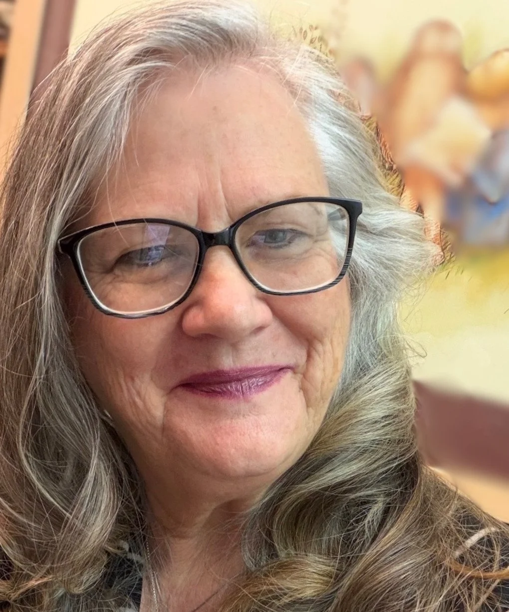kathleen Joyce, Close-up of a friendly woman with long gray hair, wearing black glasses, smiling slightly.