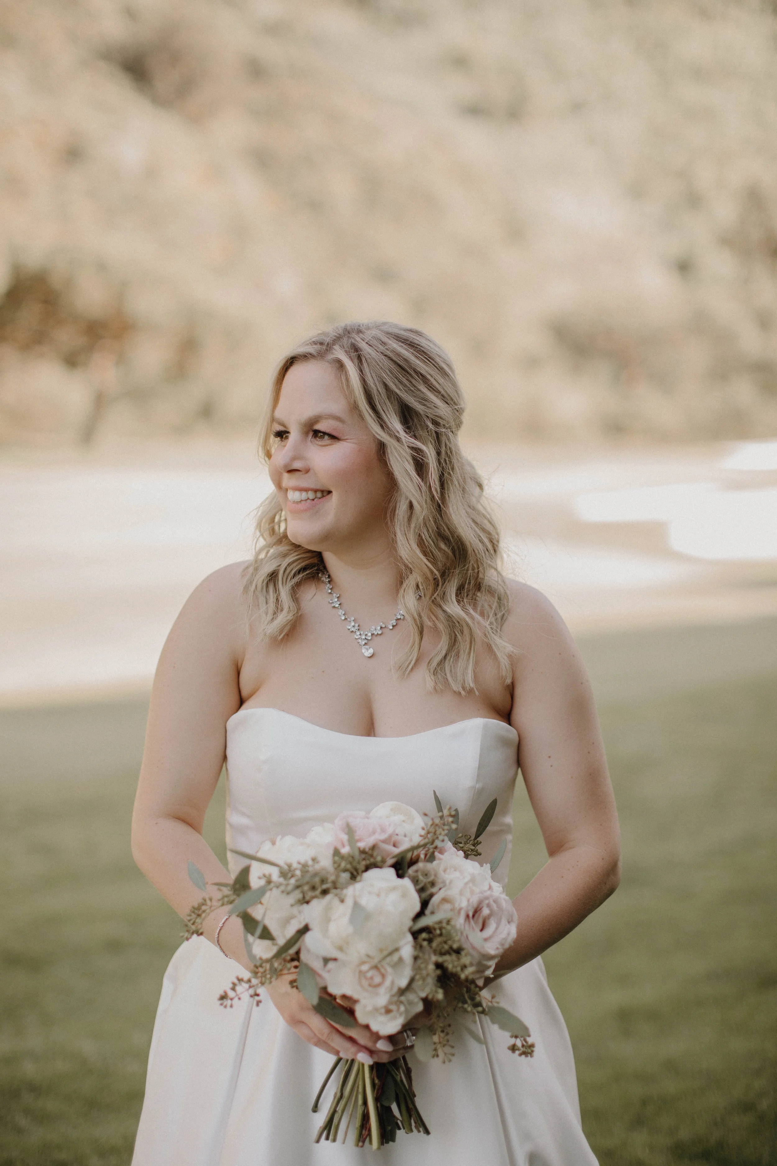 Bride with a half up hair style and soft glam makeup smiling at her bridal party