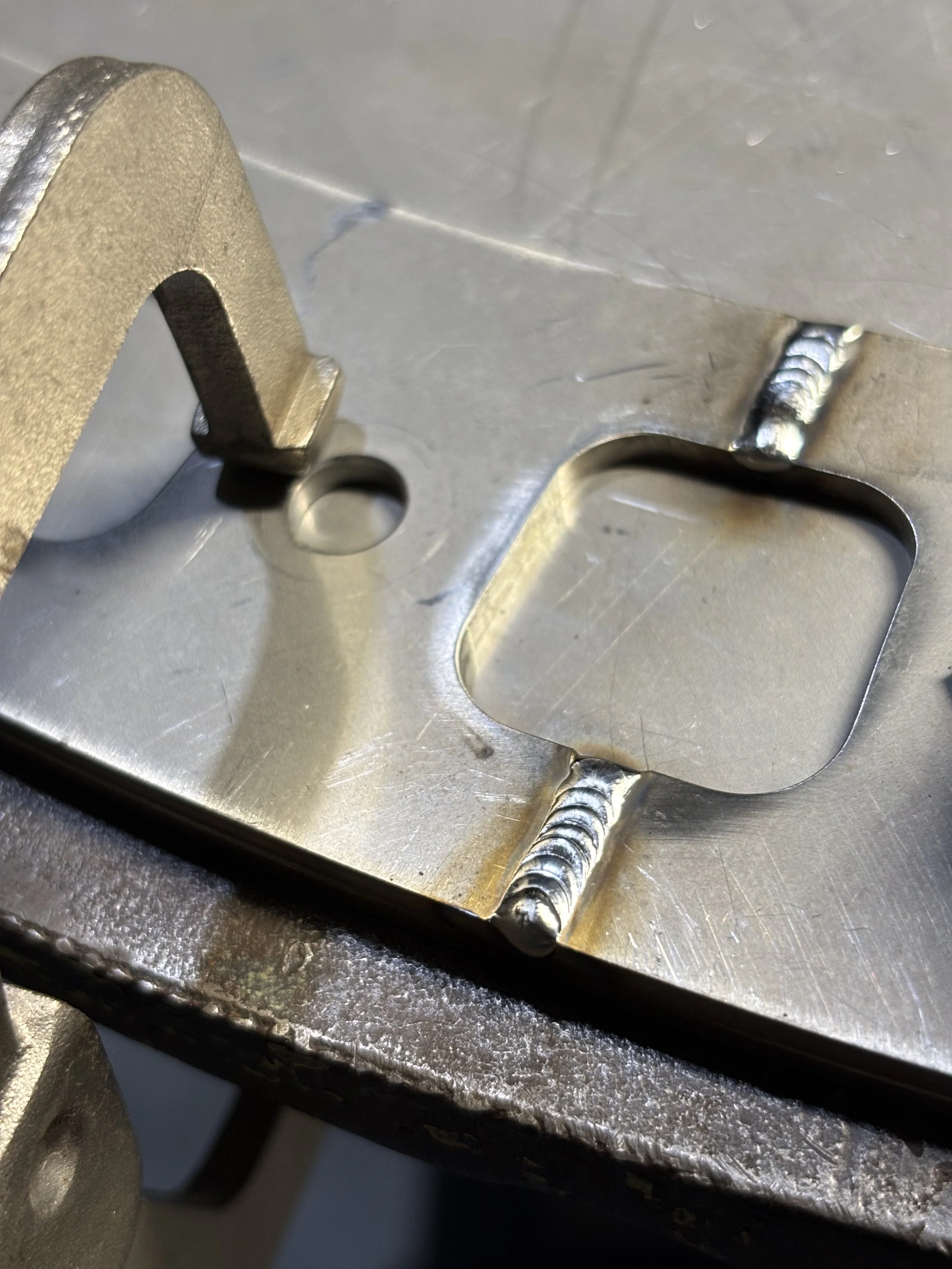 Close-up of a metallic structural component with welded joints and cutouts, likely part of a machine or assembly.