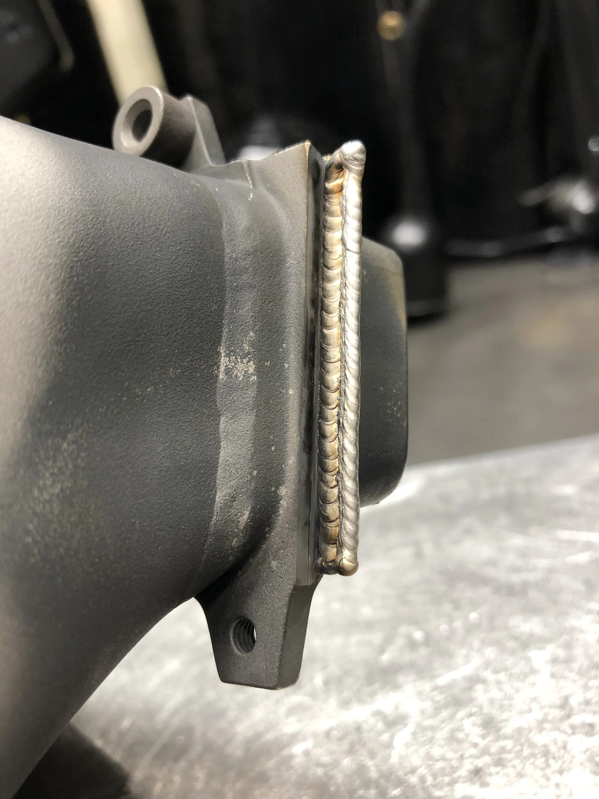 Close-up of a welded metal surface attached to a gray mechanical part.