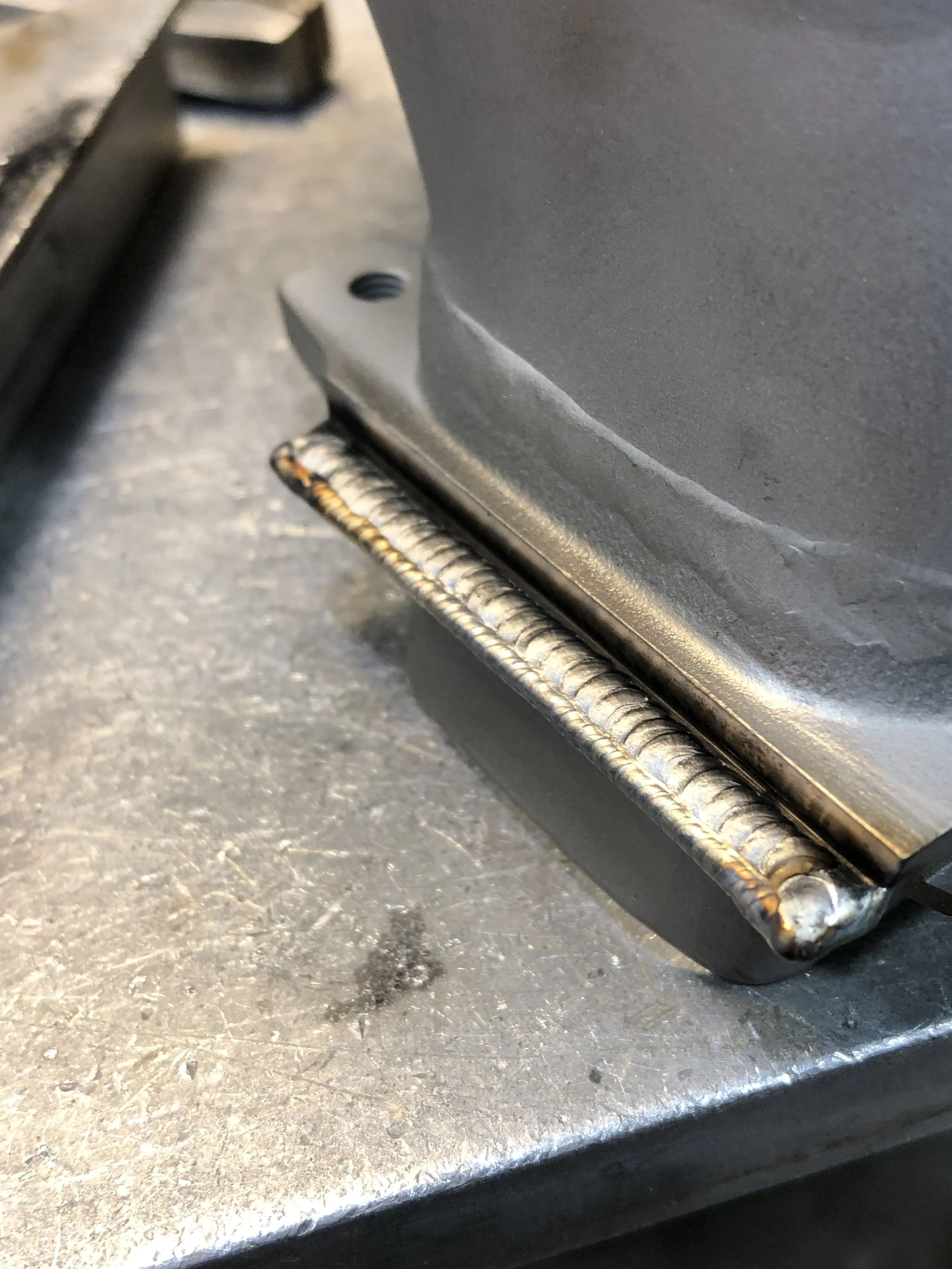 Close-up photo of a welded steel pipe and its base on a metallic surface.