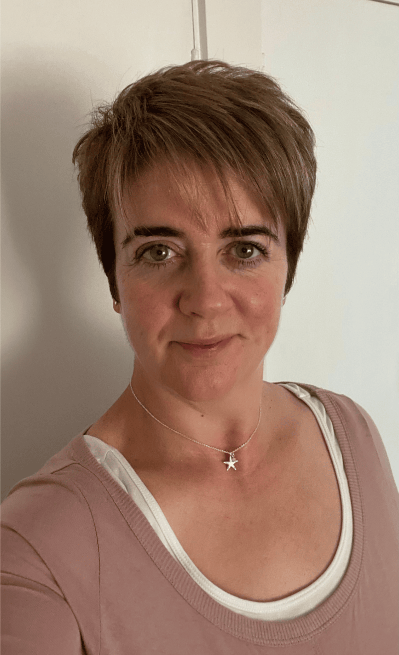 Award-winning Scottish crime author, Deborah Masson, wearing a pink top with white trim and a star-shaped necklace.