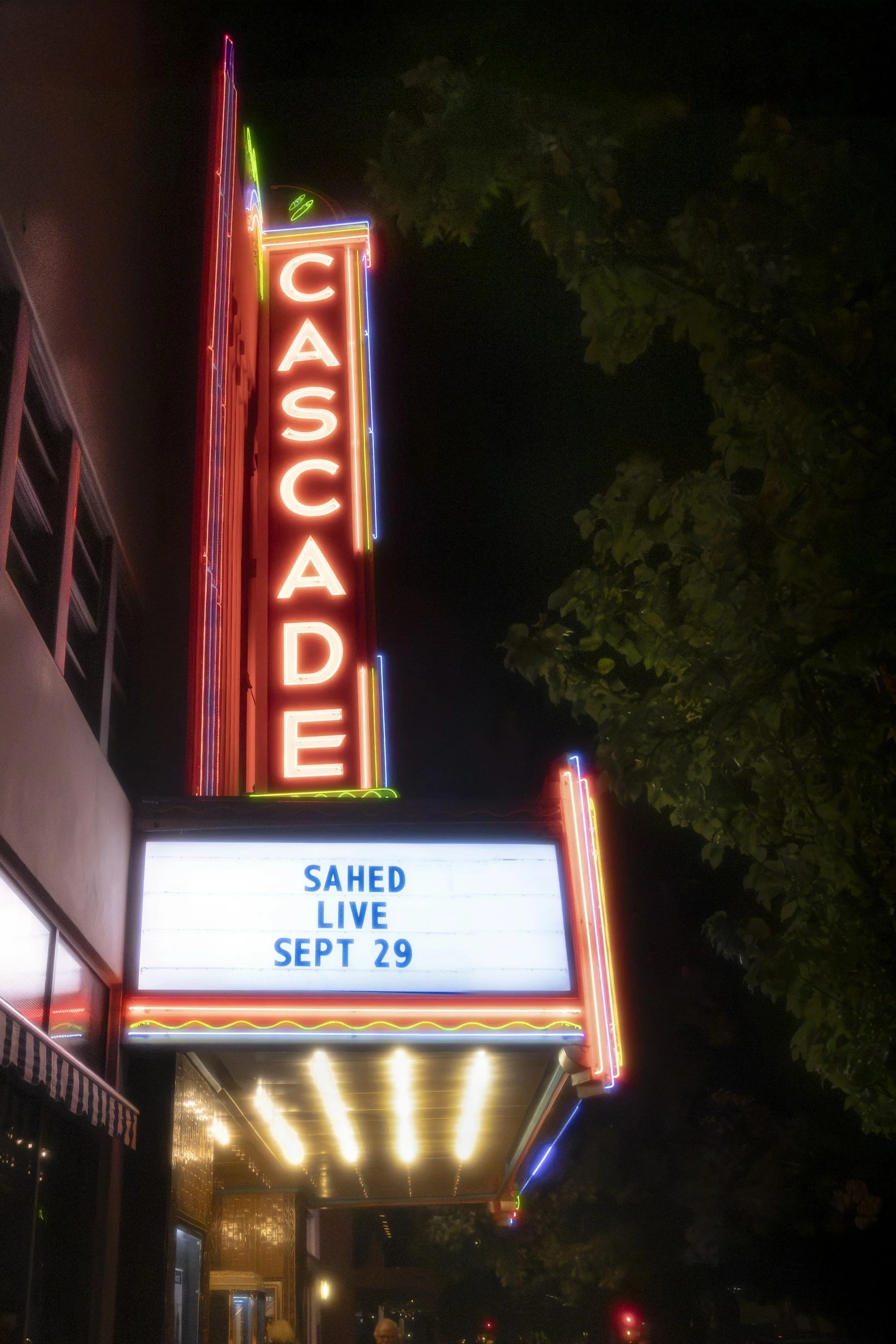 Neon sign for a cafe with the word "CAFE" in vertical red letters, along with an electronic marquee showing an upcoming live music event at Sahed on September 29.