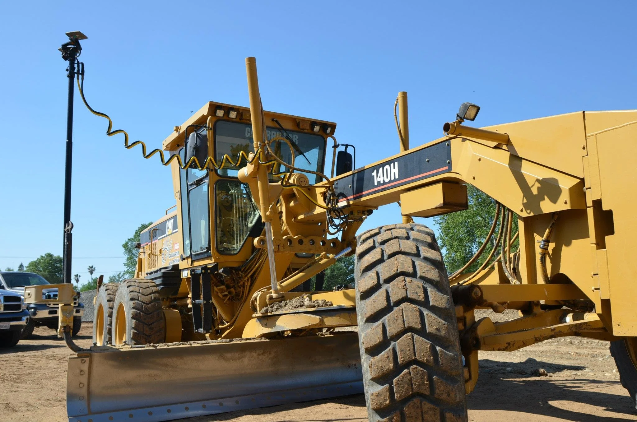 Yellow Caterpillar bulldozer with large tires parked on a dirt construction site under a clear blue sky.