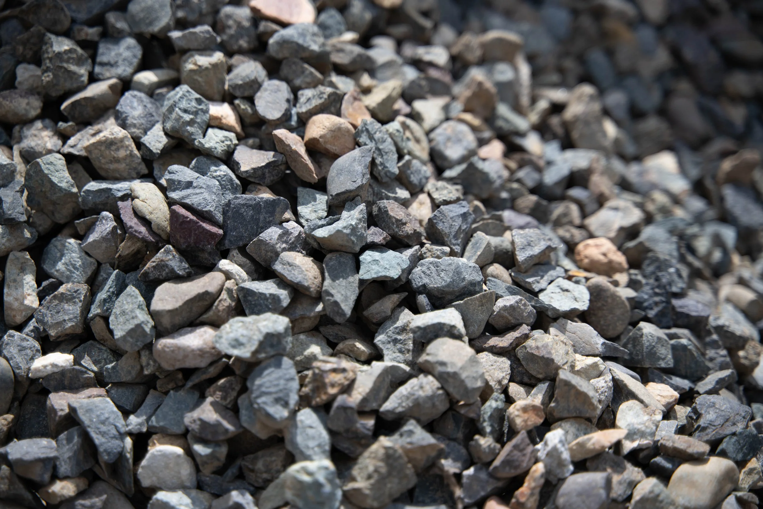 Close-up view of a pile of small, irregularly shaped gravel stones in various shades of gray, tan, and some reddish hues.