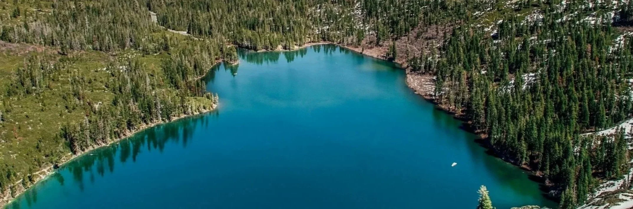 Aerial view of a blue lake surrounded by dense green pine forest and rocky terrain.