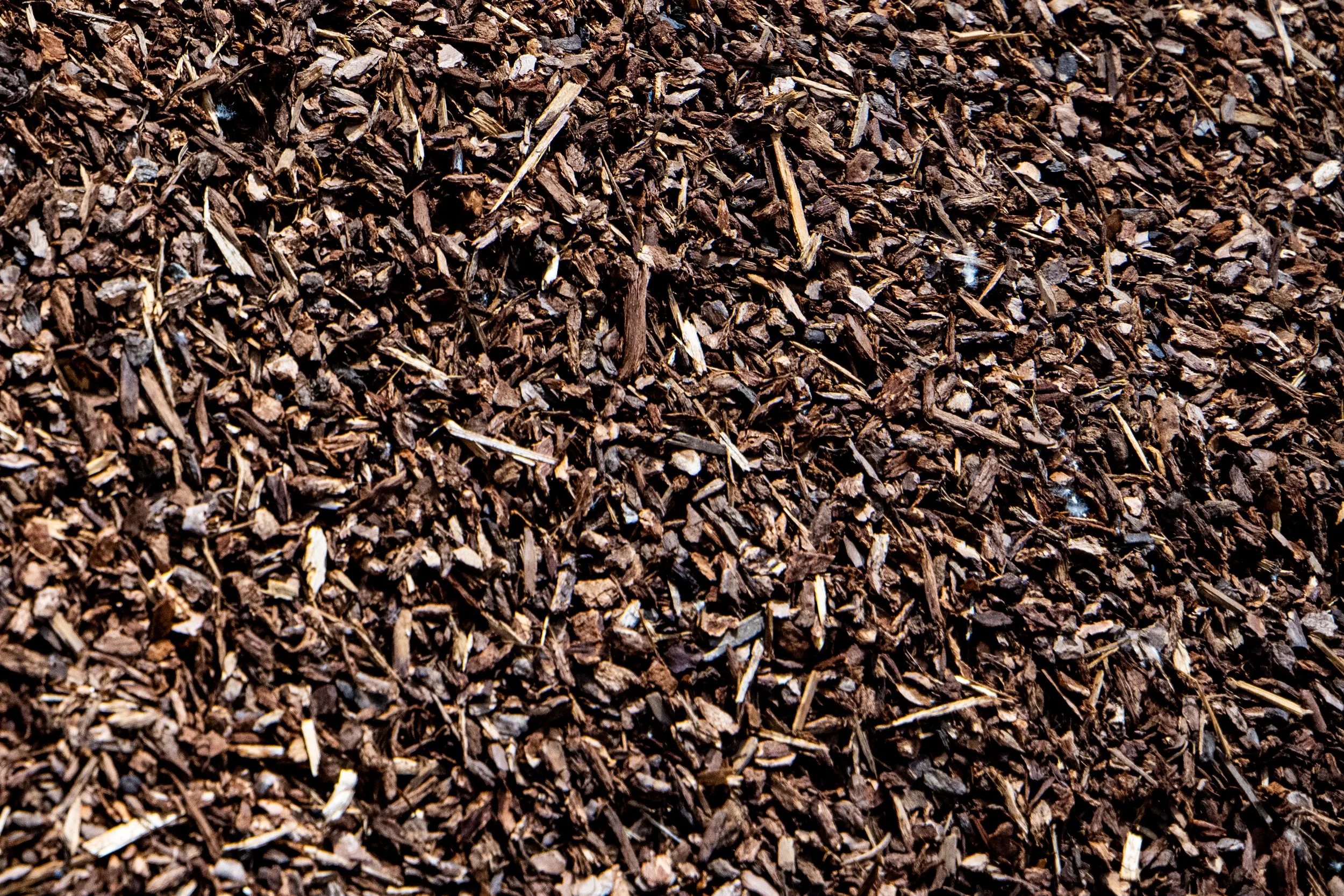 A close-up image of brown wood mulch or shredded bark, used as ground cover in landscaping or gardening.