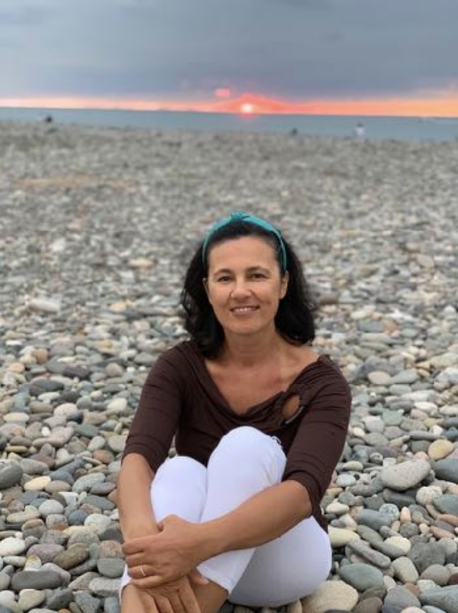 Marina of HopeWell Reiki sitting on a rocky beach at sunset