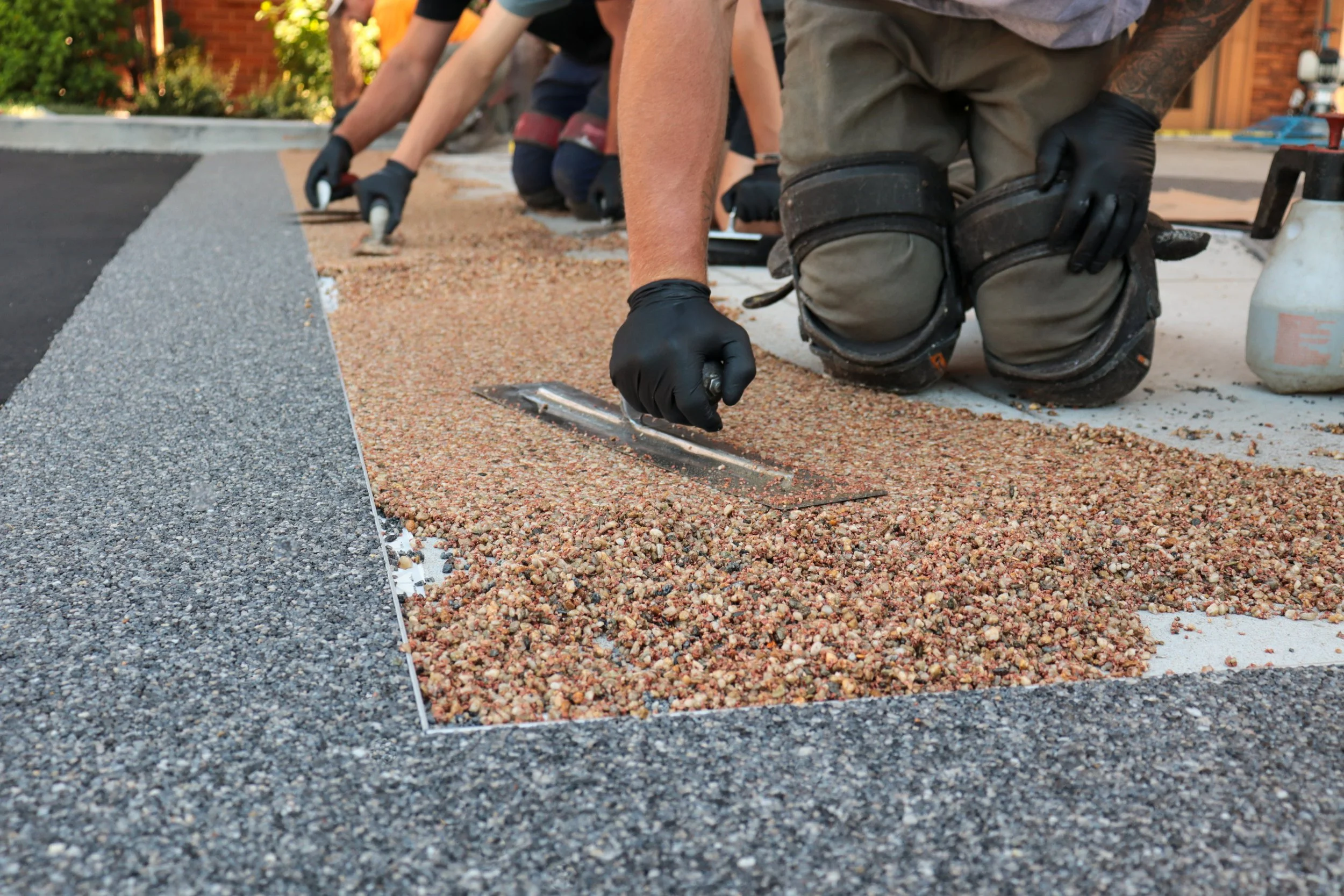 People kneeling on the ground and installing a layer of colored gravel for a landscaping project outside.