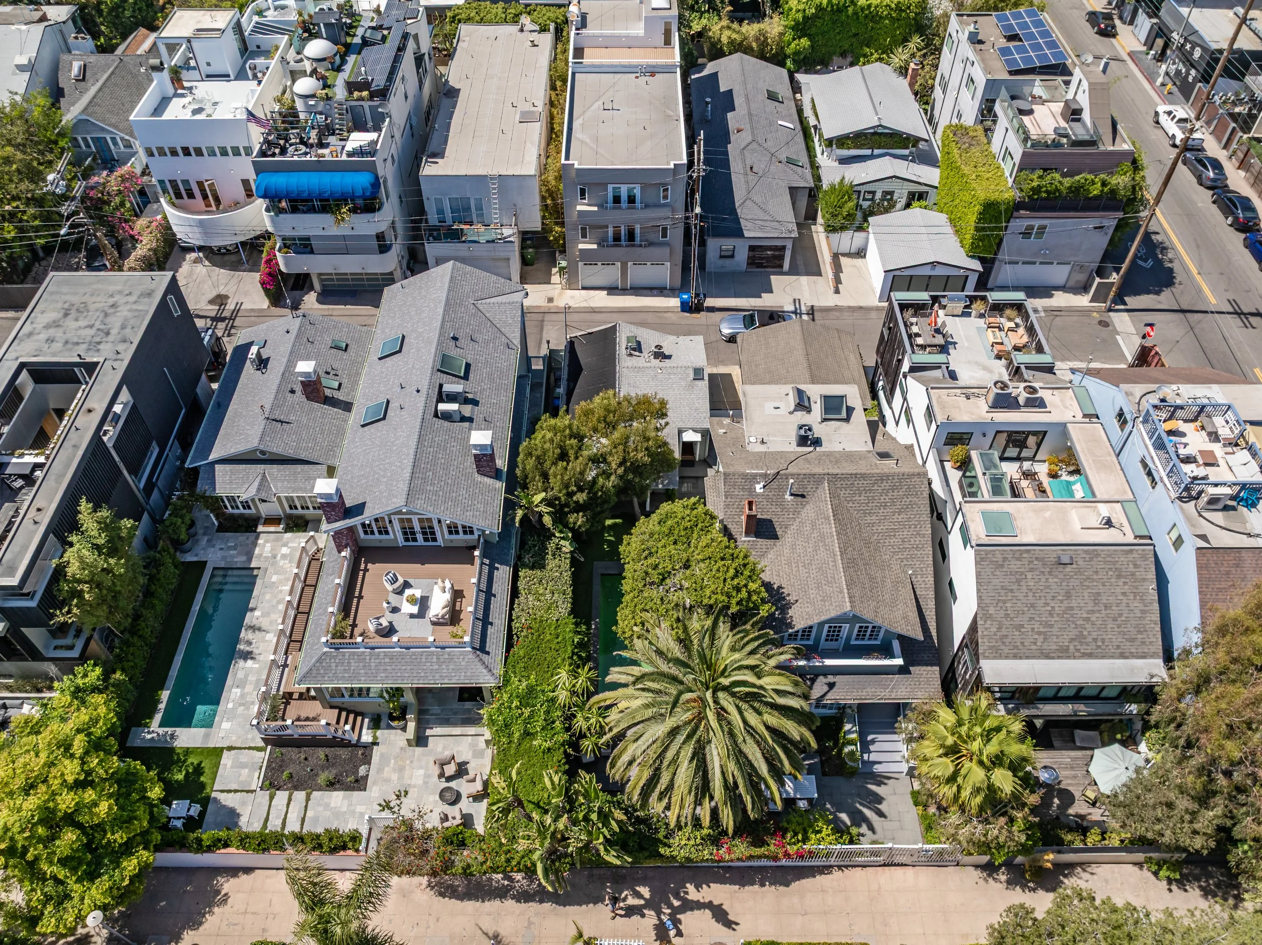 An aerial view of a dense neighborhood with houses, greenery, trees, and parked cars along the streets.
