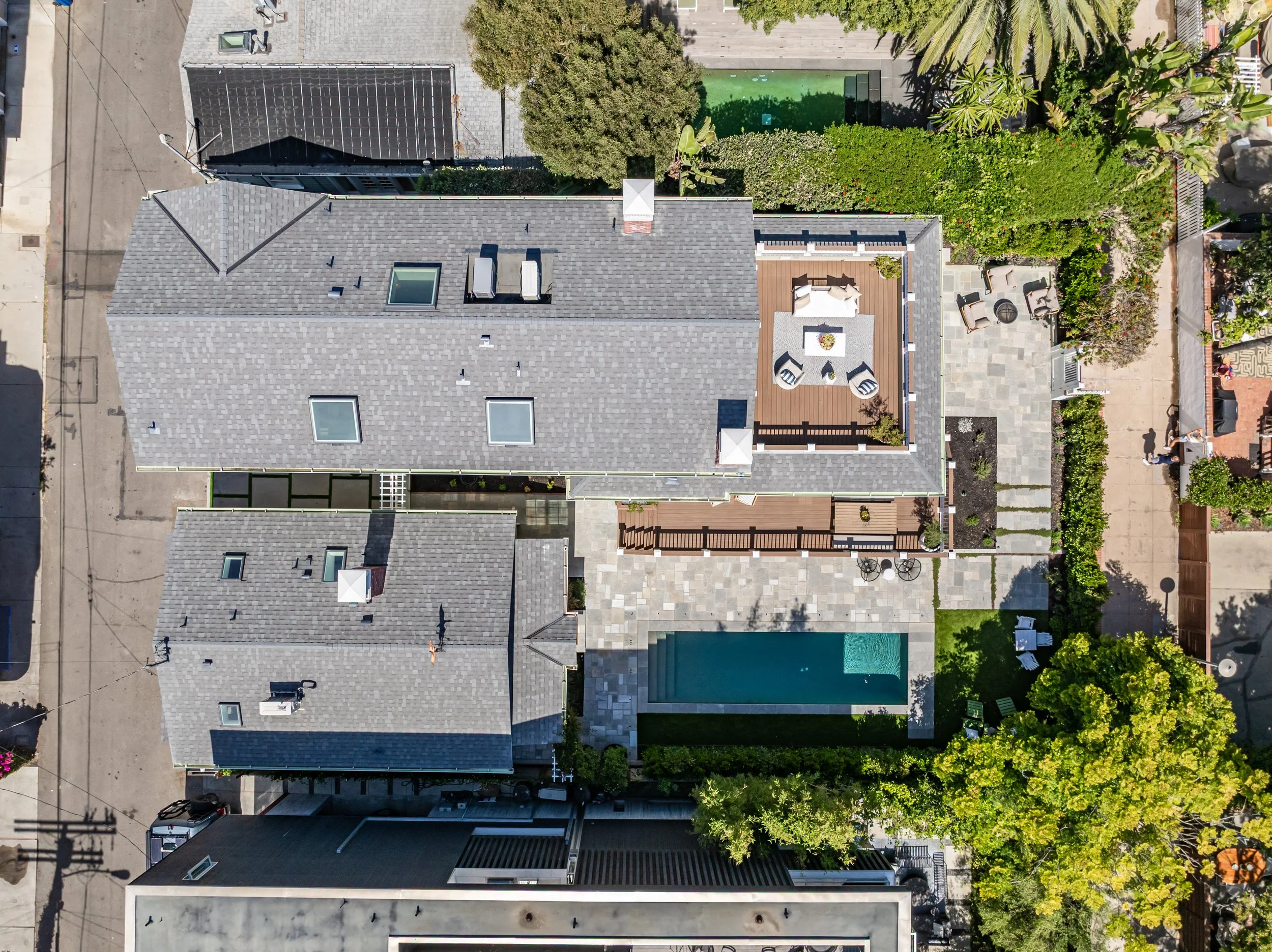 Aerial view of residential houses with gray roofs, a backyard with outdoor seating and a small pool, and trees providing greenery.
