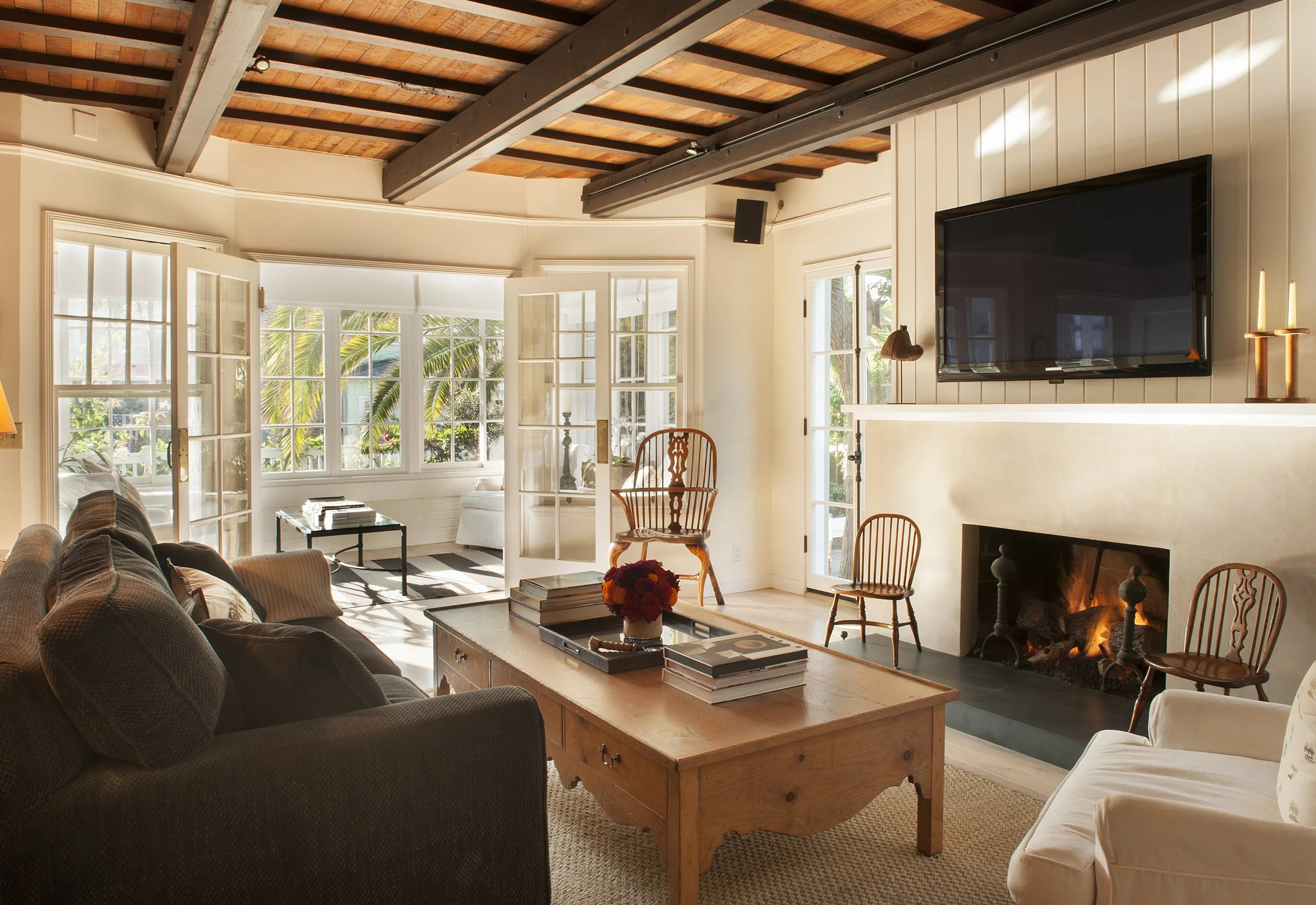 Living room with large windows, wooden ceiling beams, fireplace, and various chairs and sofas.