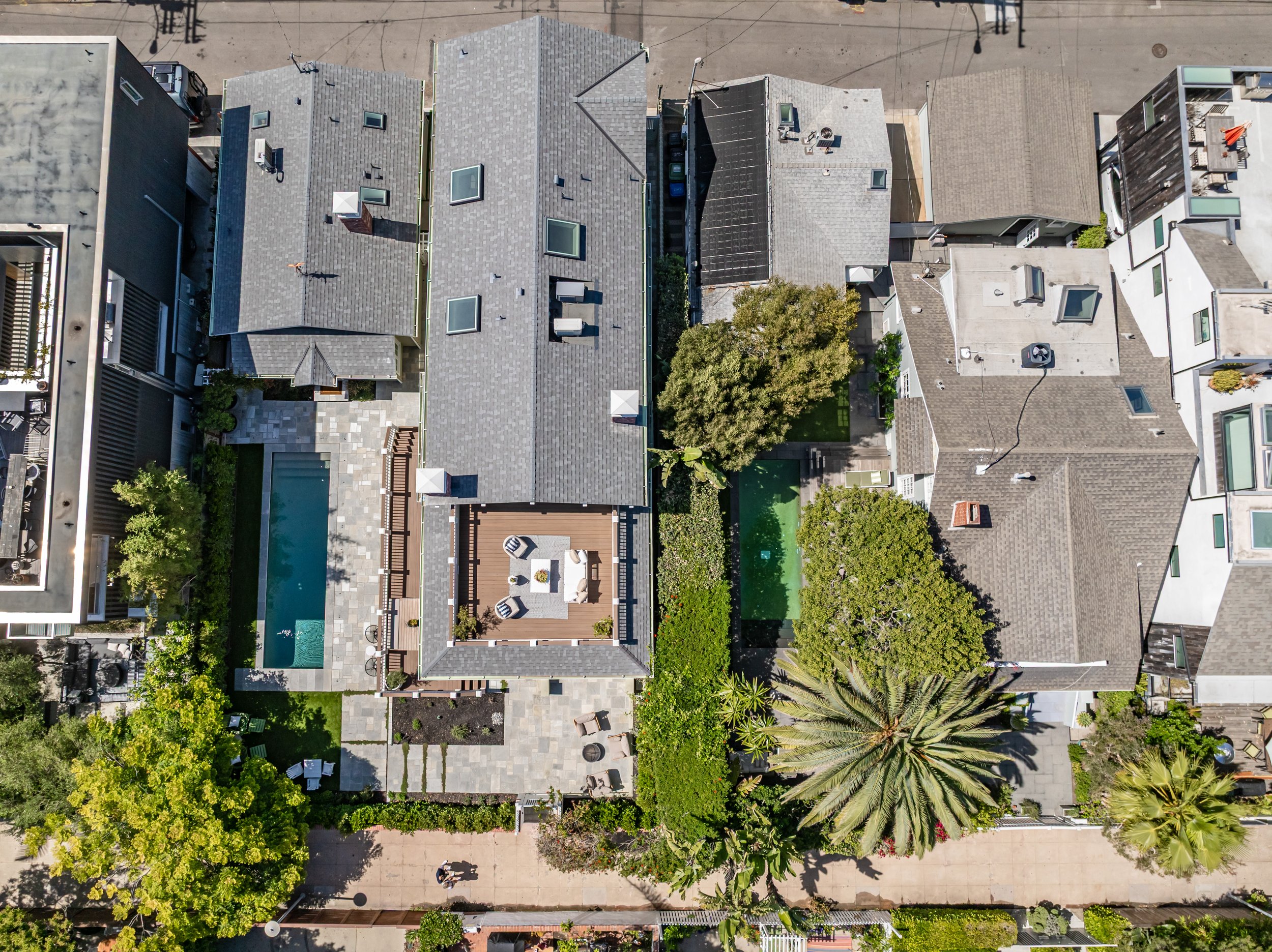 An aerial view of a neighborhood with multiple houses, a backyard with a pool, trees, and gardens.