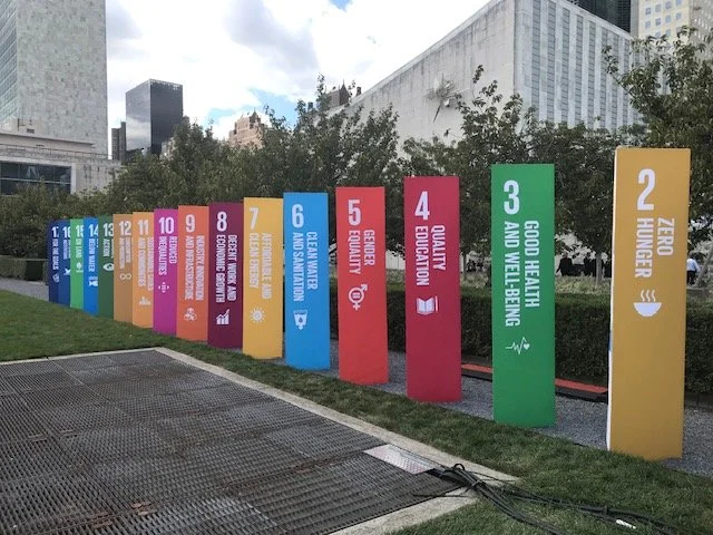 Colorful signs listing sustainable development goals, numbered 1 to 17, displayed outdoors in an urban area.