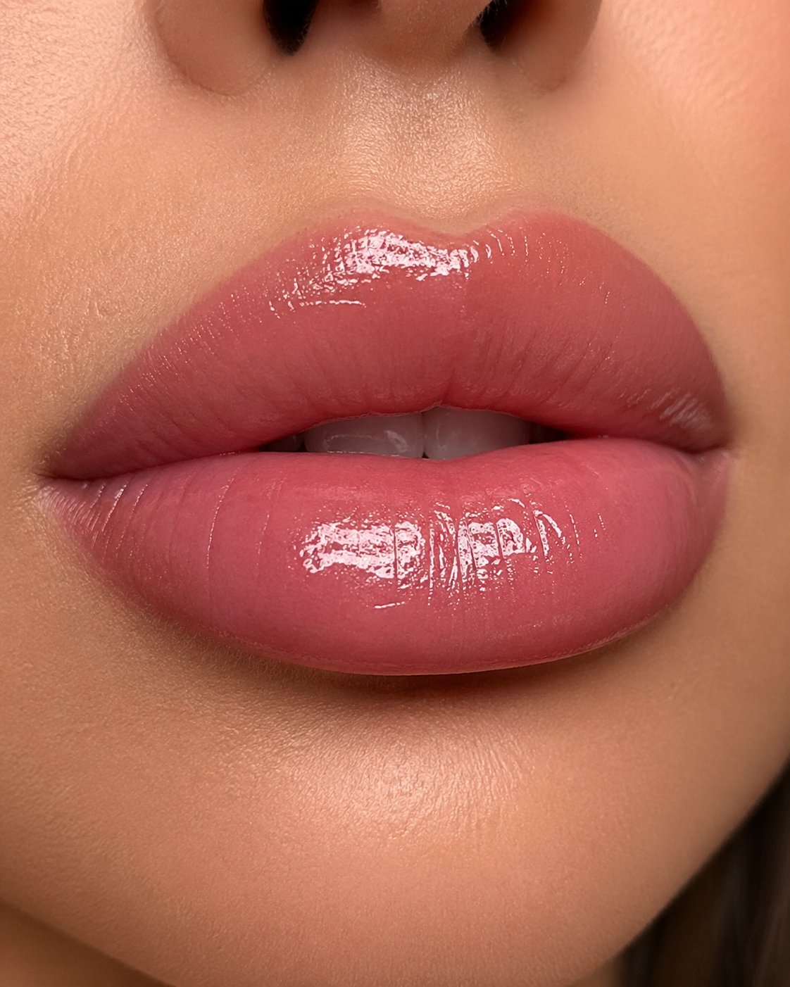 Close-up of a person's lips with pink lipstick and gloss, slightly parted revealing part of the teeth.